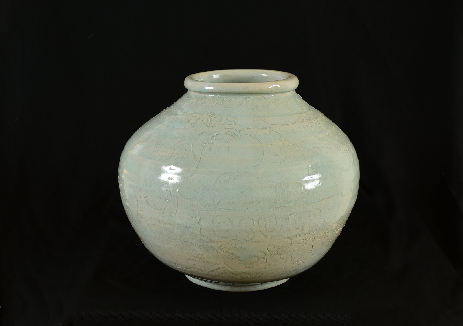 A pale green ceramic jar with embossed floral patterns against a black background.