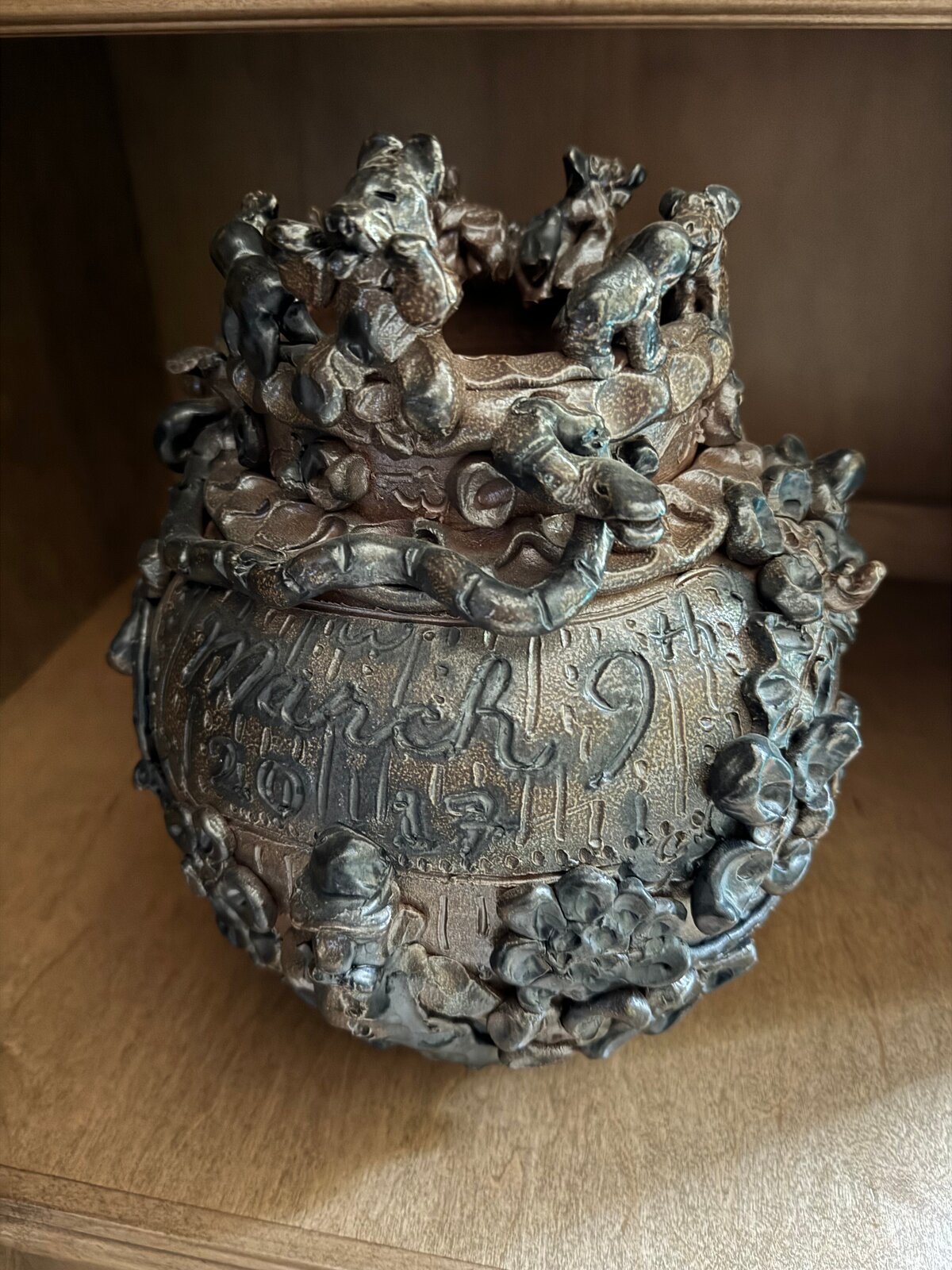 A dark, textured ceramic vessel with a grotesque face and crown-like top.