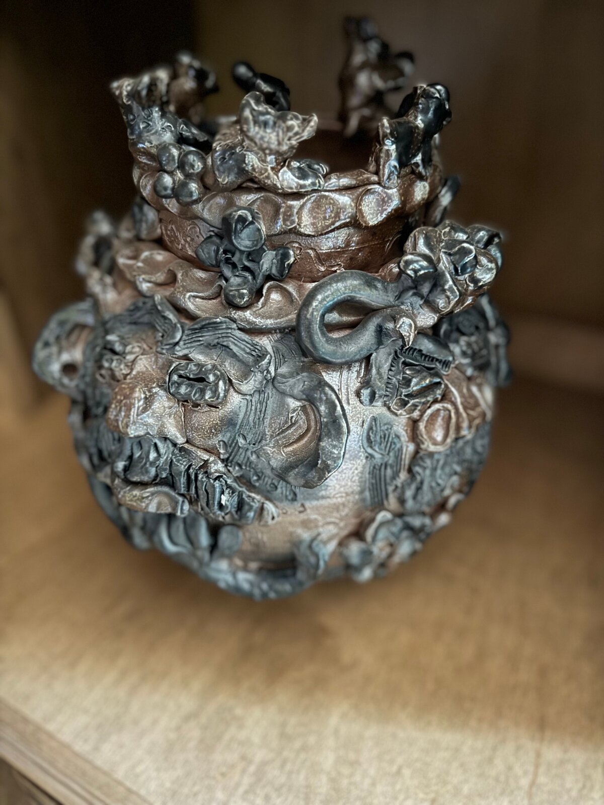 A dark, textured ceramic vessel with a grotesque face and crown-like top.