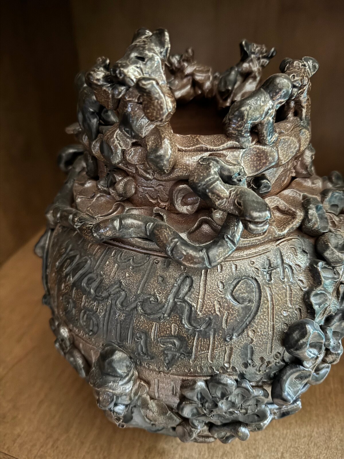 A dark, textured ceramic vessel with a grotesque face and crown-like top.