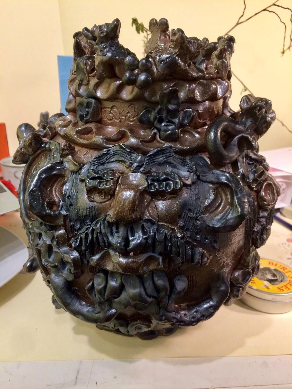 A dark, textured ceramic vessel with a grotesque face and crown-like top.
