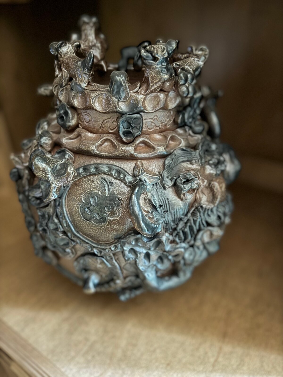 A dark, textured ceramic vessel with a grotesque face and crown-like top.