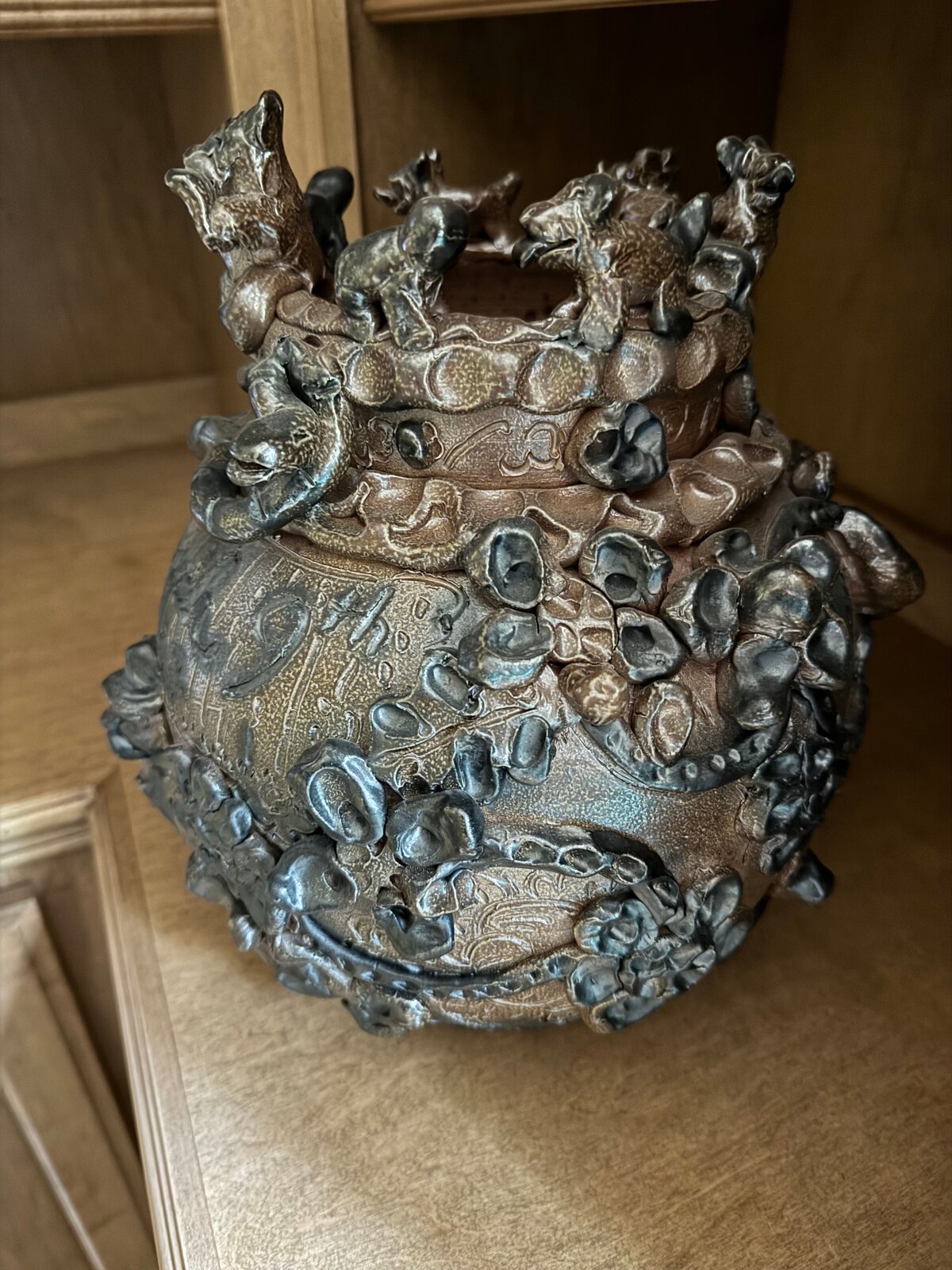 A dark, textured ceramic vessel with a grotesque face and crown-like top.