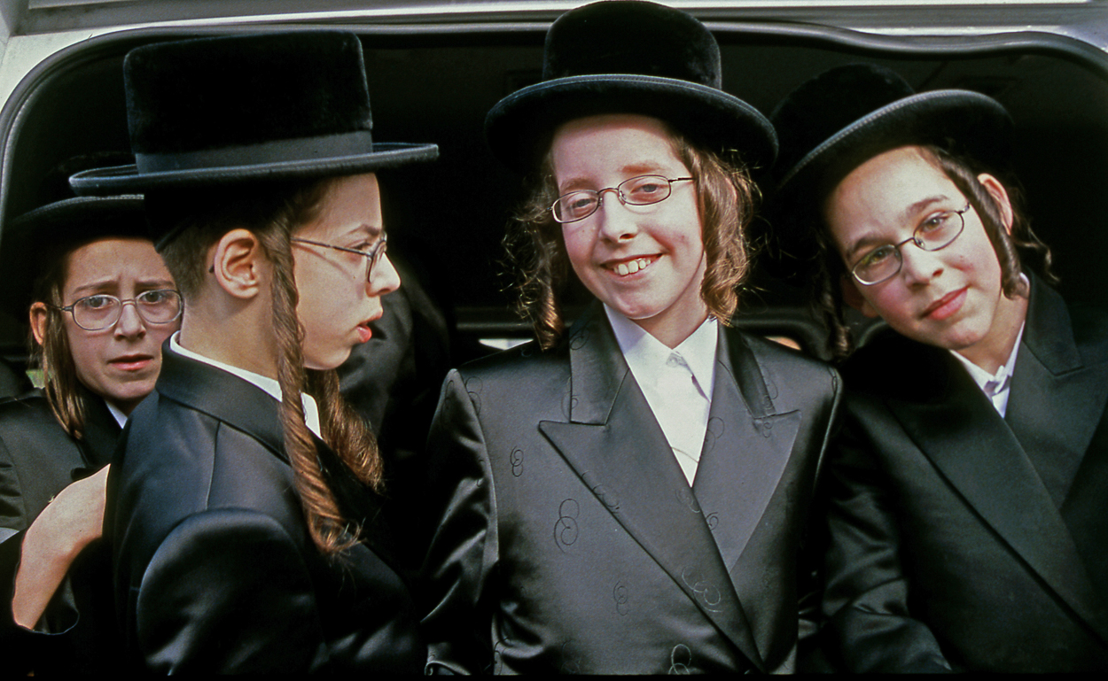 A group of young boys in suits and hats sitting in the back of a car.