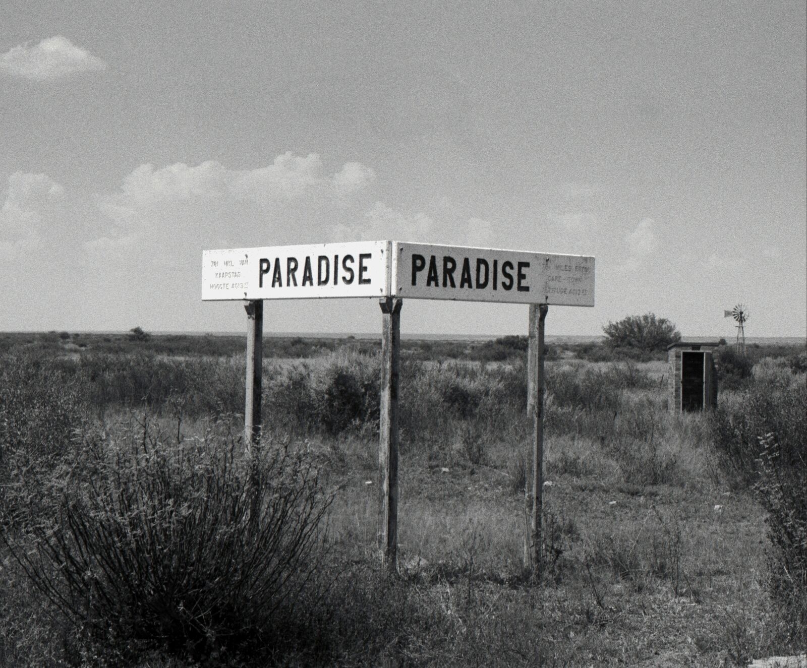 A black and white photo of a sign that says "Paradise" in the middle of a field.