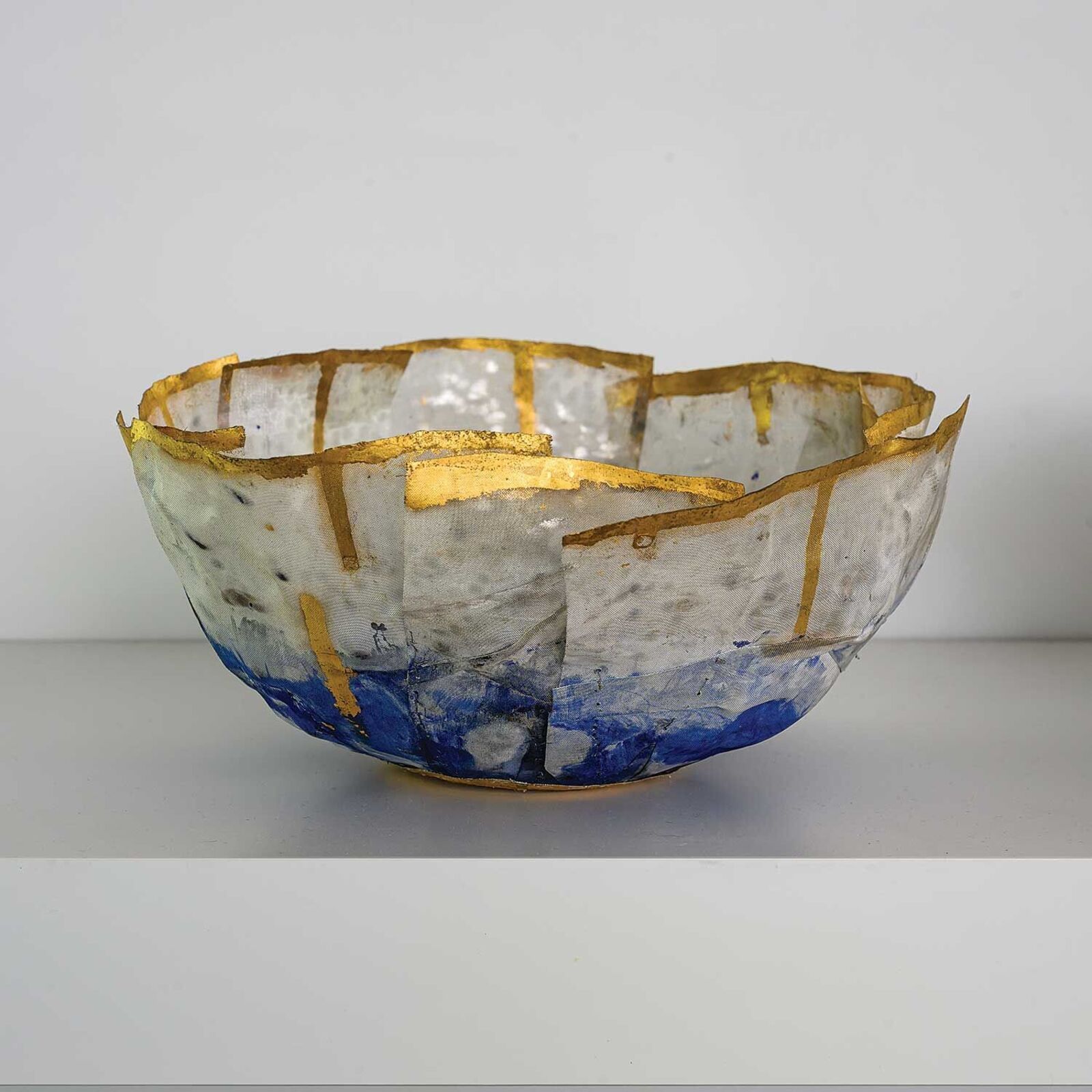 A sculptural bowl featuring a translucent, layered texture with gold leaf accents and blue washes.