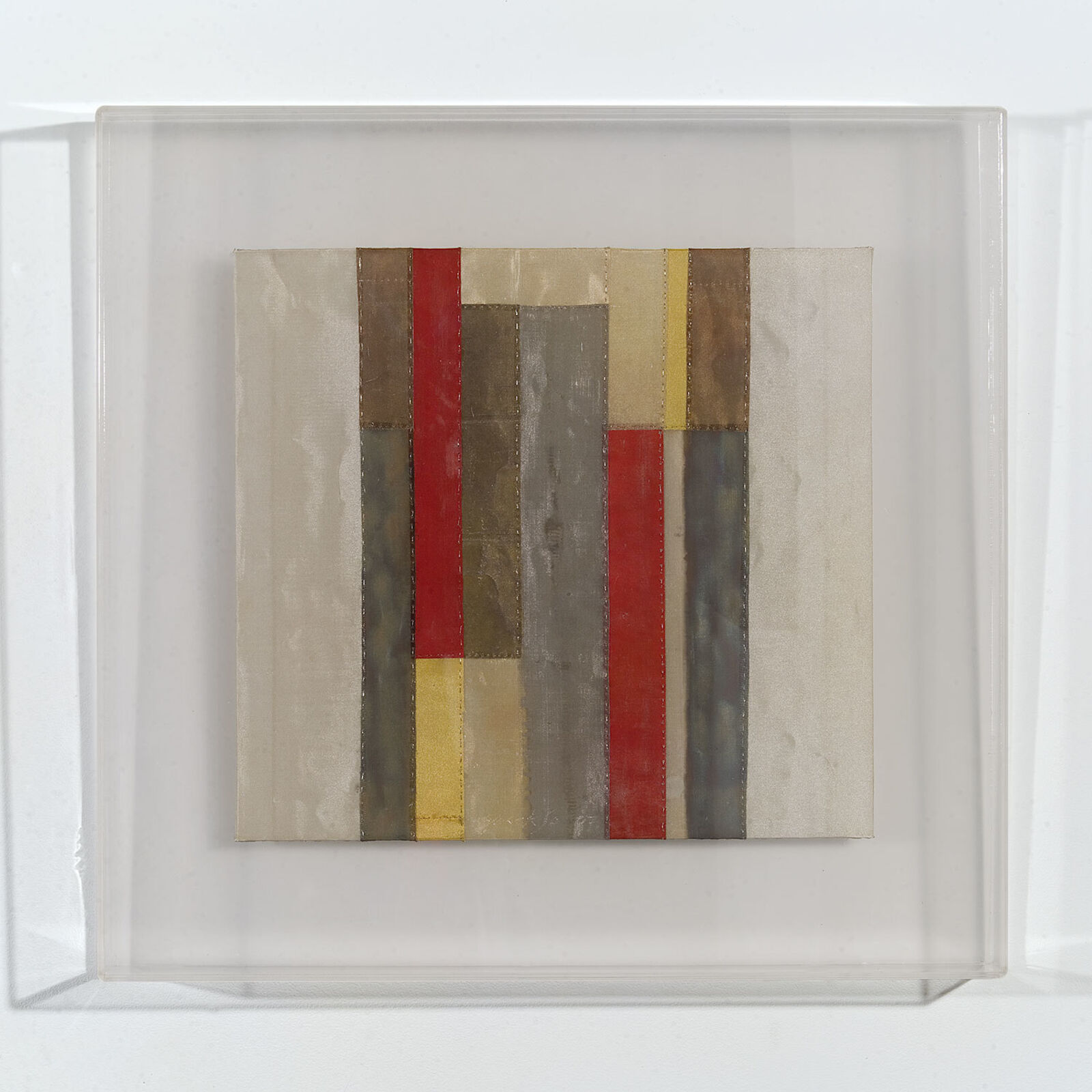 A minimalist textile artwork featuring vertical strips of fabric in muted earth tones and bold red.