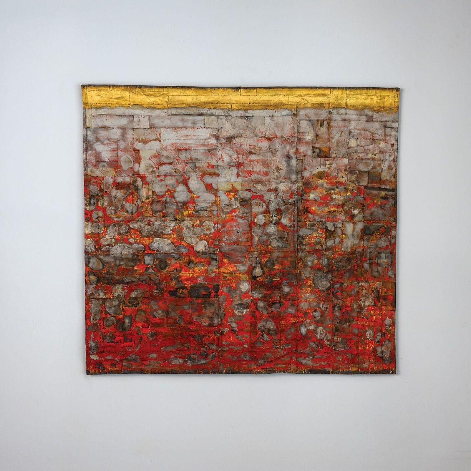 A textured abstract painting with red and gold tones hangs on a white wall in an industrial-style room.
