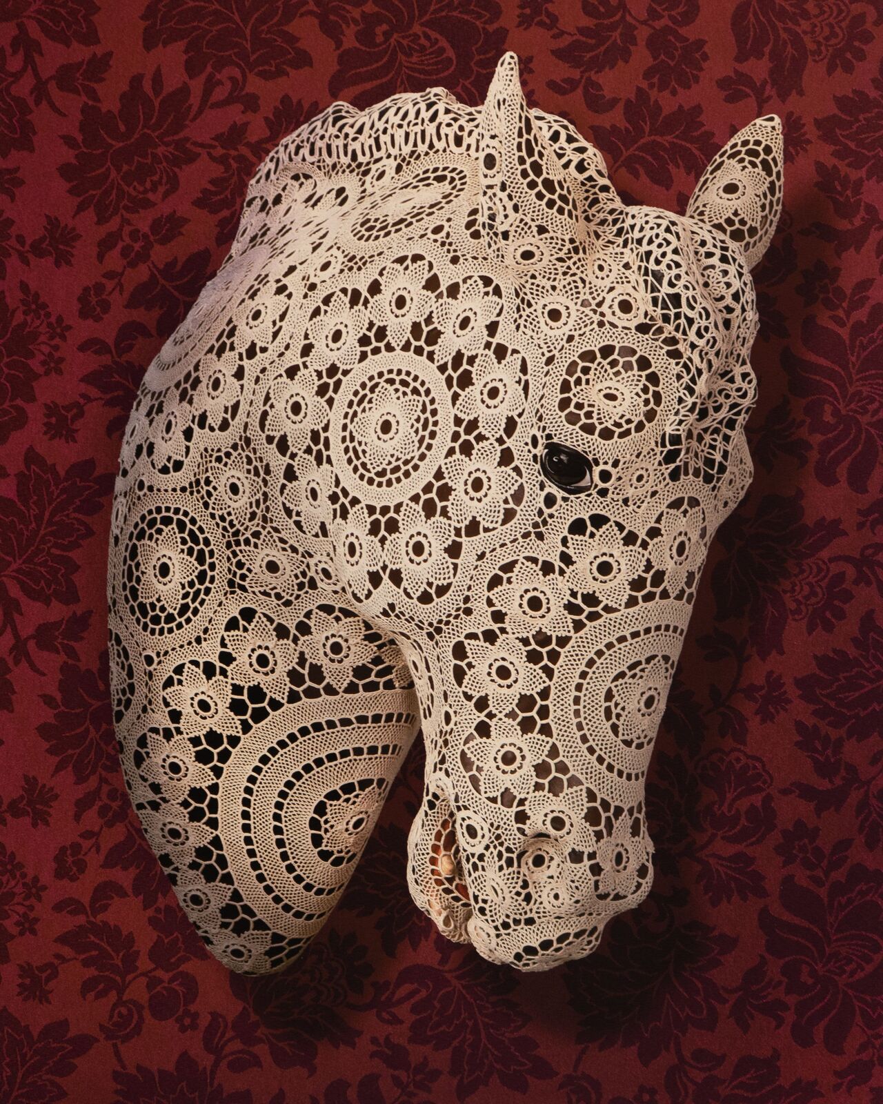A white lace horse head mounted on a dark floral background.