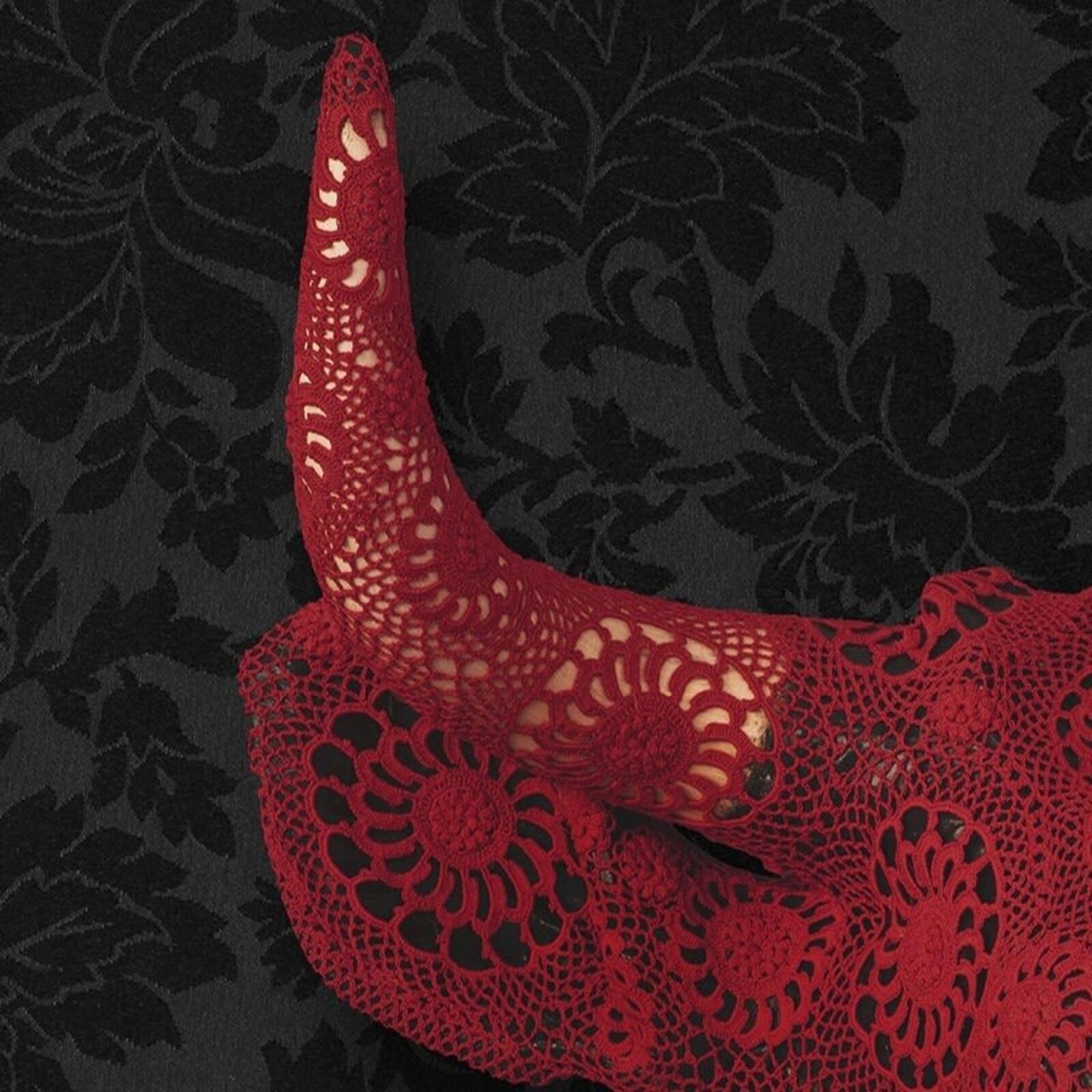 A striking red bull skull covered in intricate lace against a dark floral background.