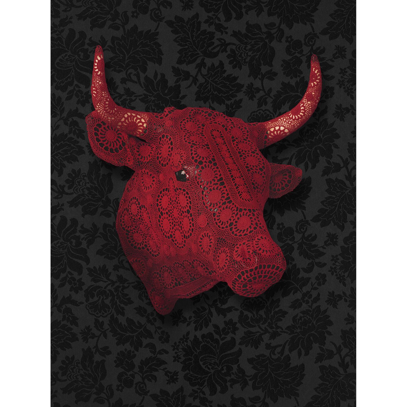 A striking red bull skull covered in intricate lace against a dark floral background.