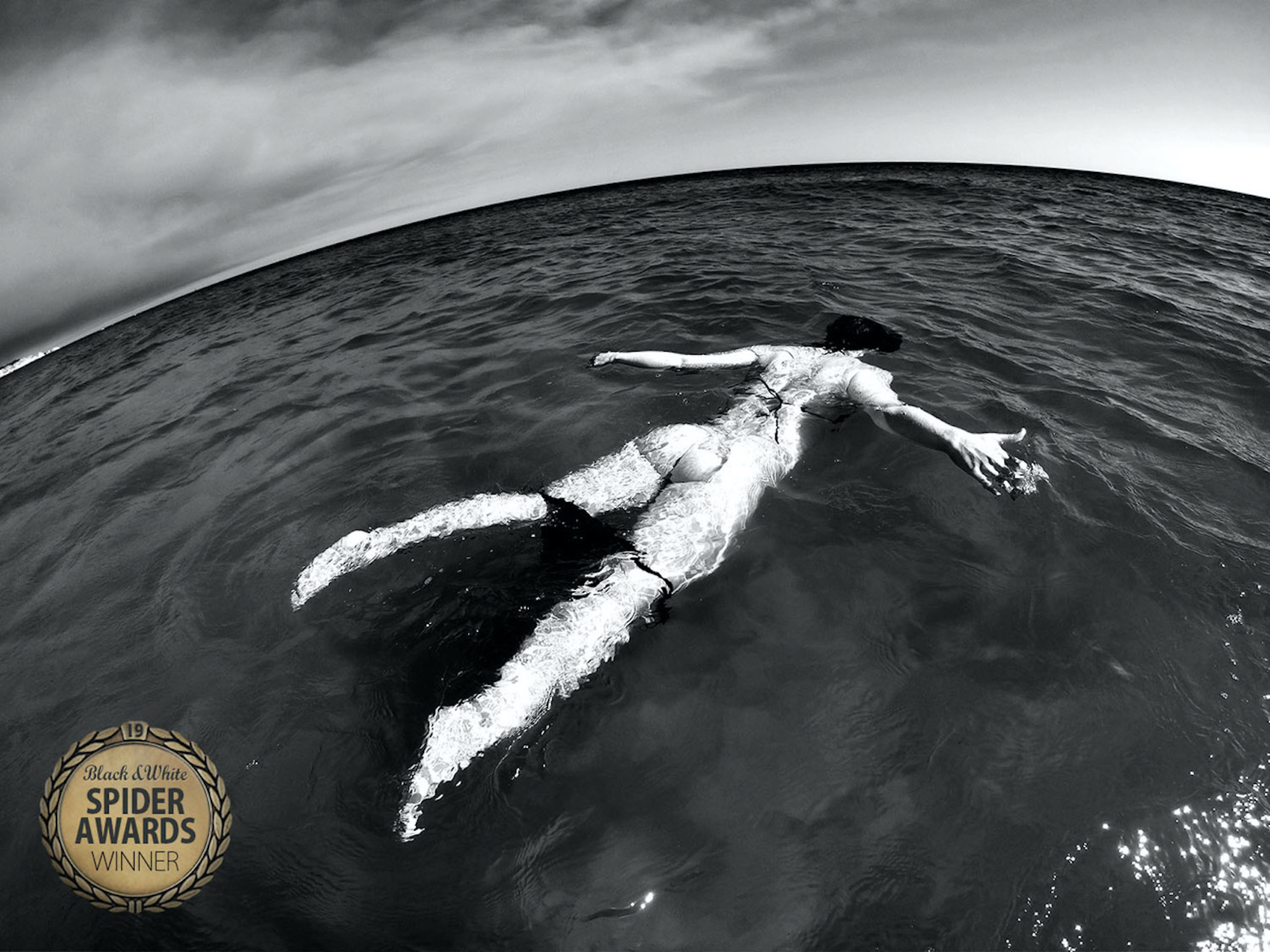 A black and white photo of a mermaid floating in the ocean.