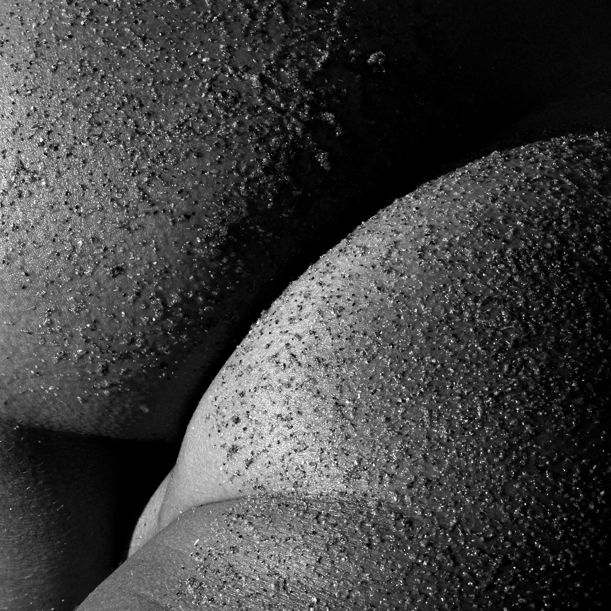 A black and white photo of a woman's butt covered in sand.