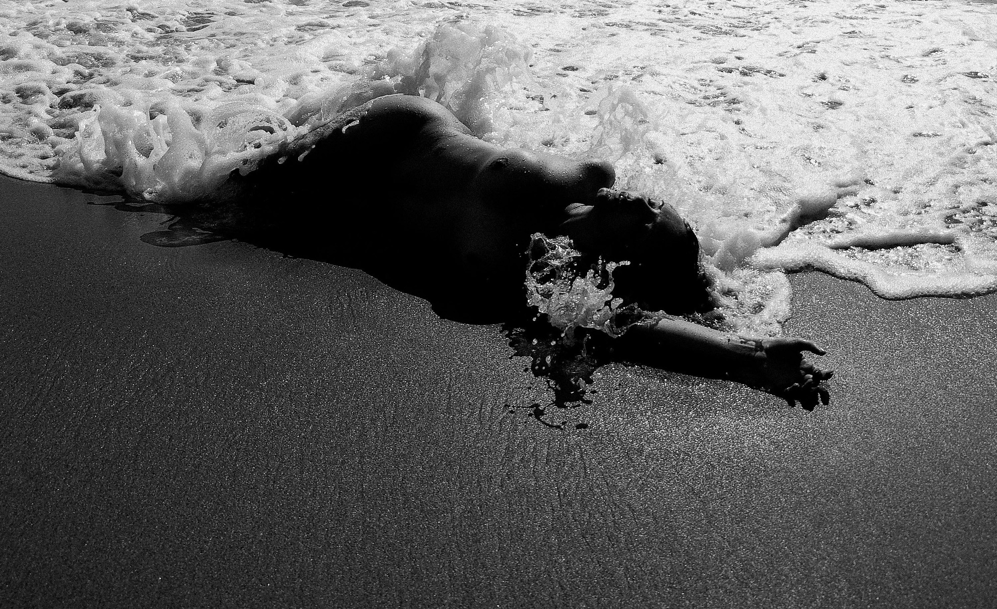 A black and white photo of a woman laying in the water.