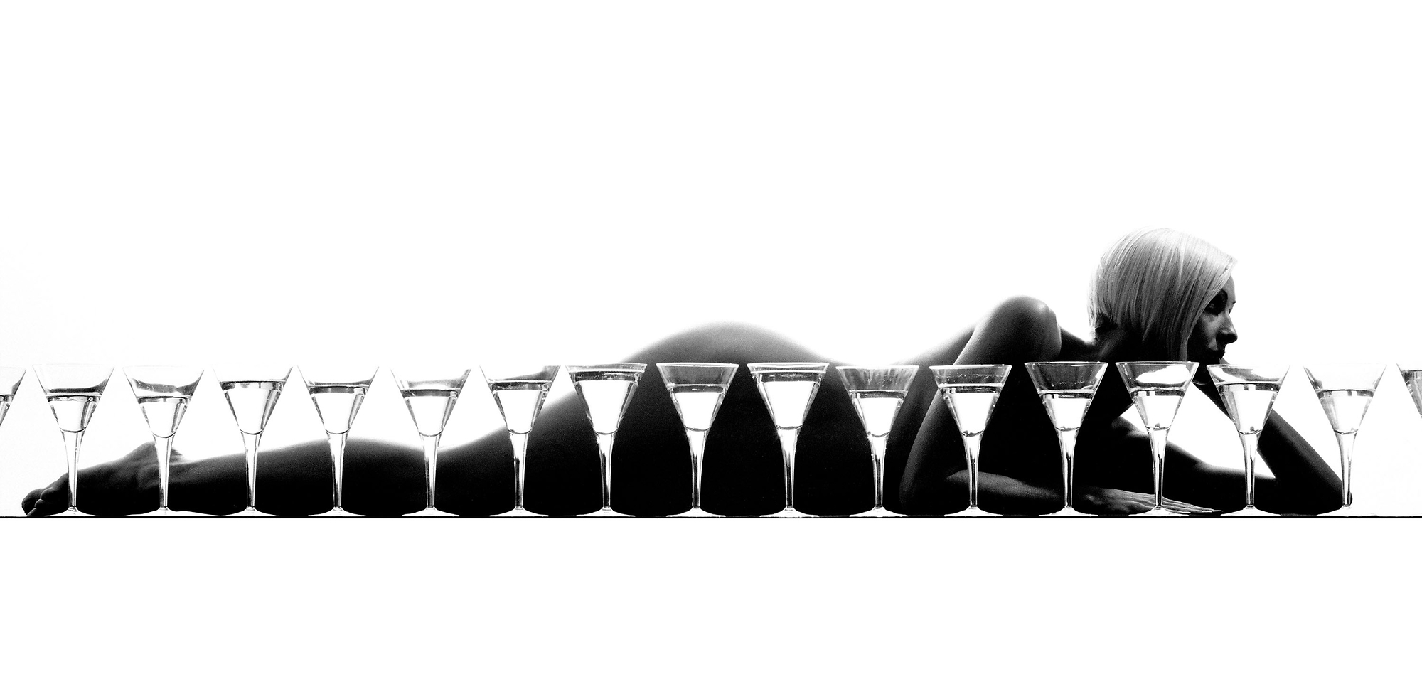 A woman laying on the ground next to a row of empty glasses.