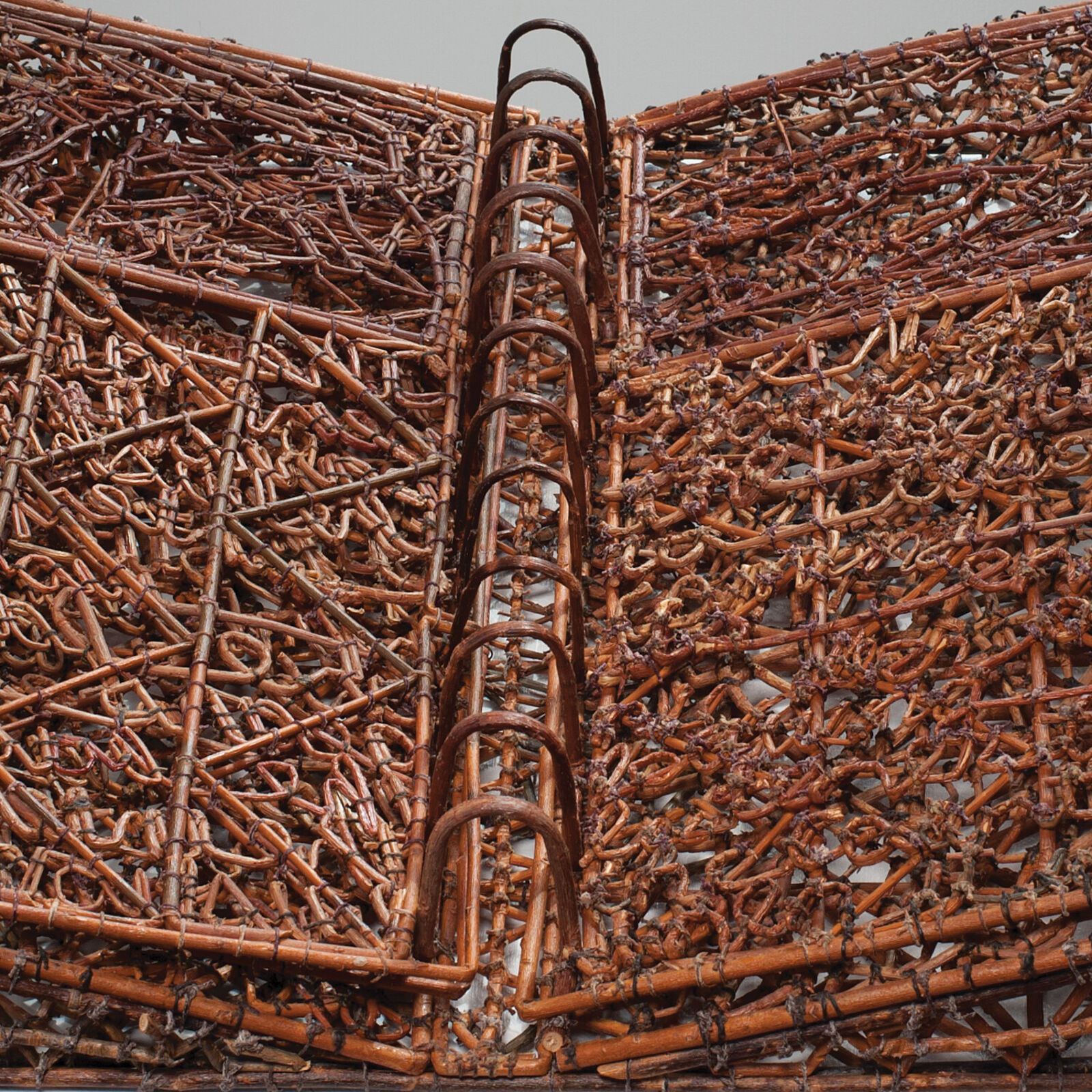 A sculptural book made of woven twigs and metal rings sits open on a white pedestal.