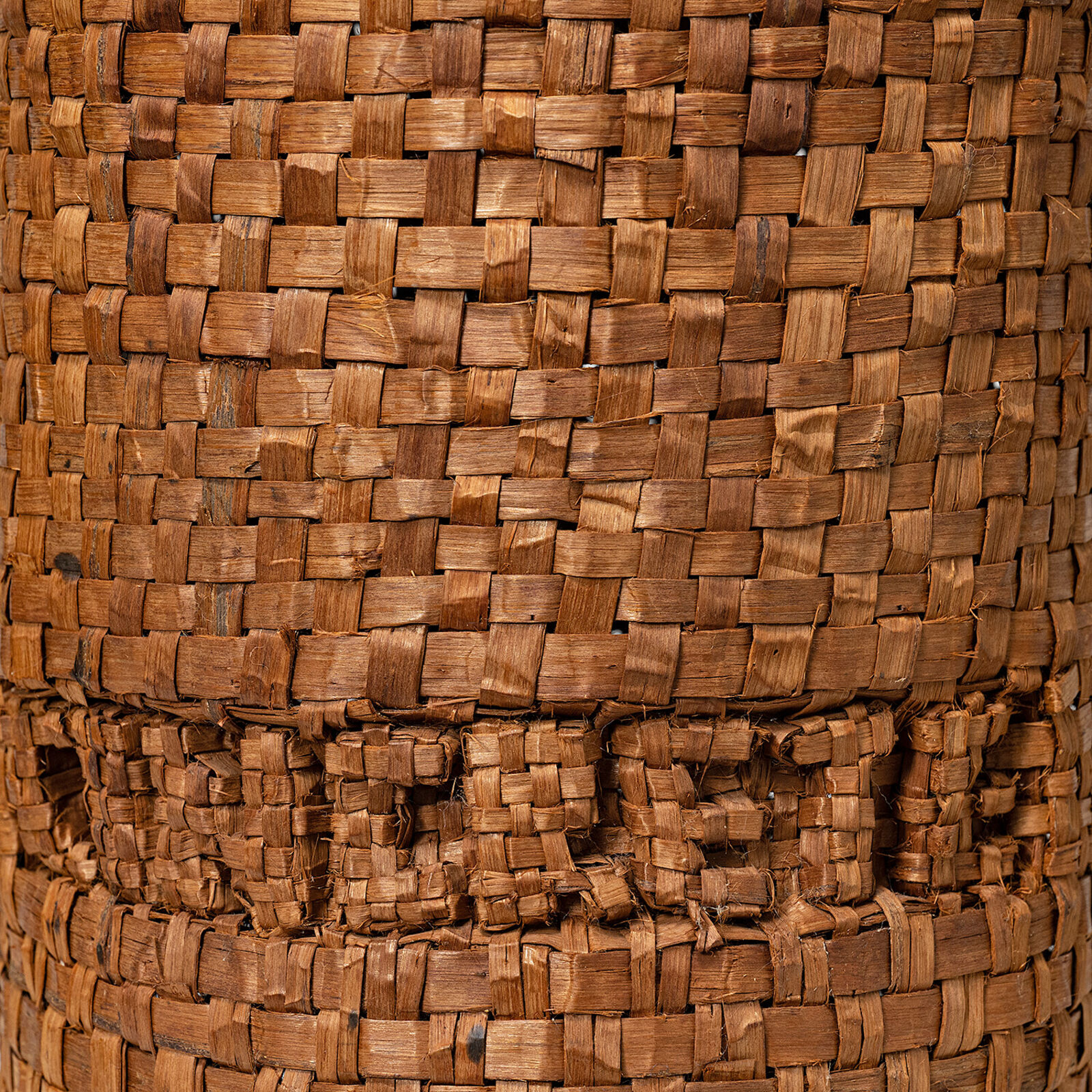 A tall woven basket sculpture wrapped with dark branches, displayed on a white pedestal.