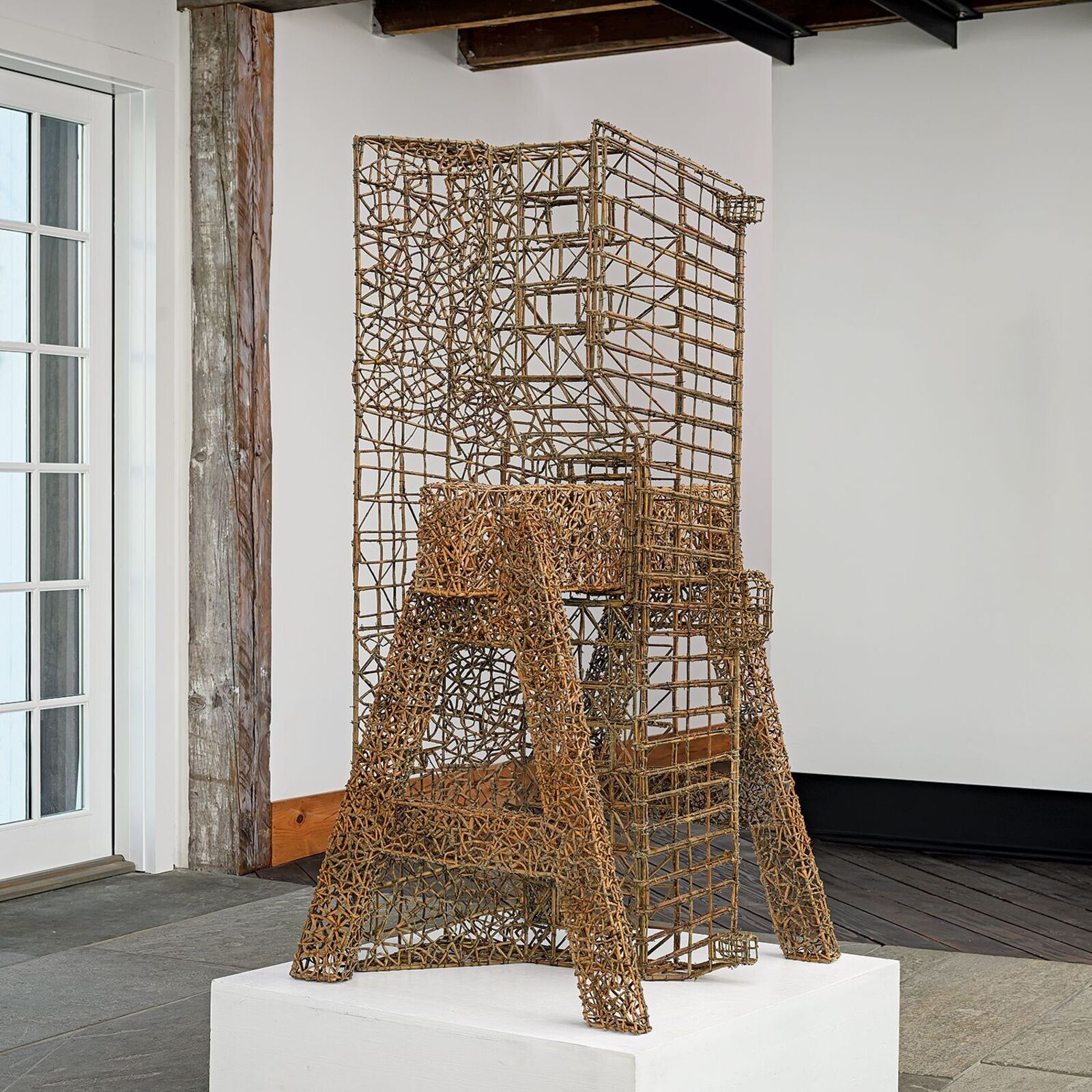 A wireframe sculpture of the Eiffel Tower standing on a wooden floor between metal railings.