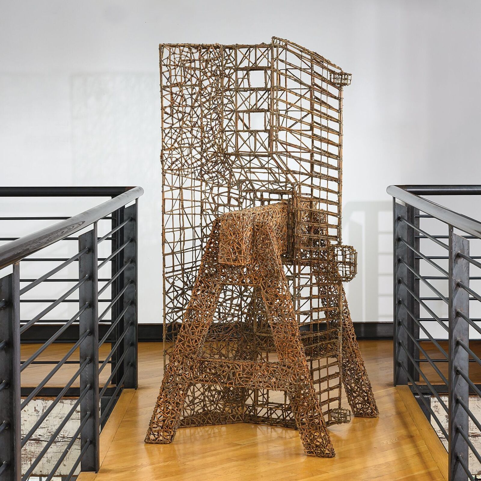 A wireframe sculpture of the Eiffel Tower standing on a wooden floor between metal railings.
