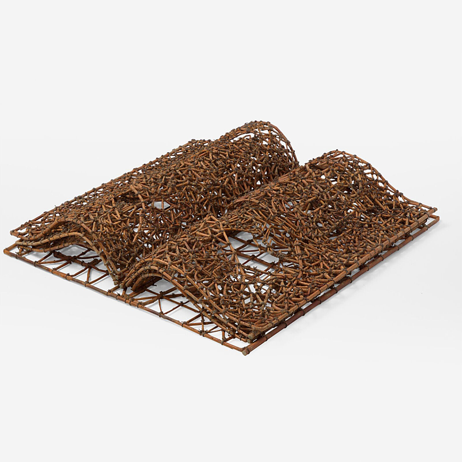 A sculptural book made of woven twigs sits on a white surface beneath a window.