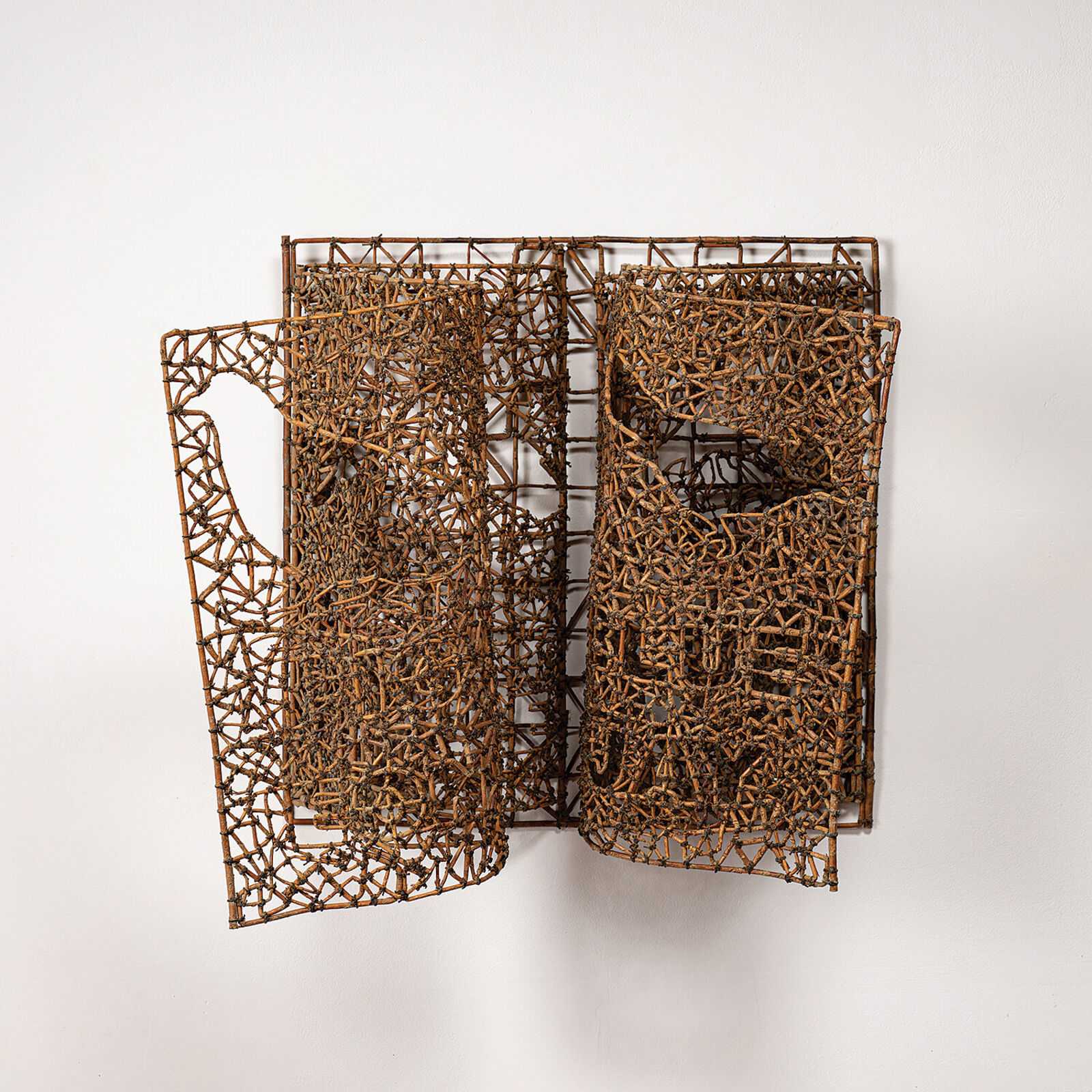 A sculptural book made of woven twigs sits on a white surface beneath a window.