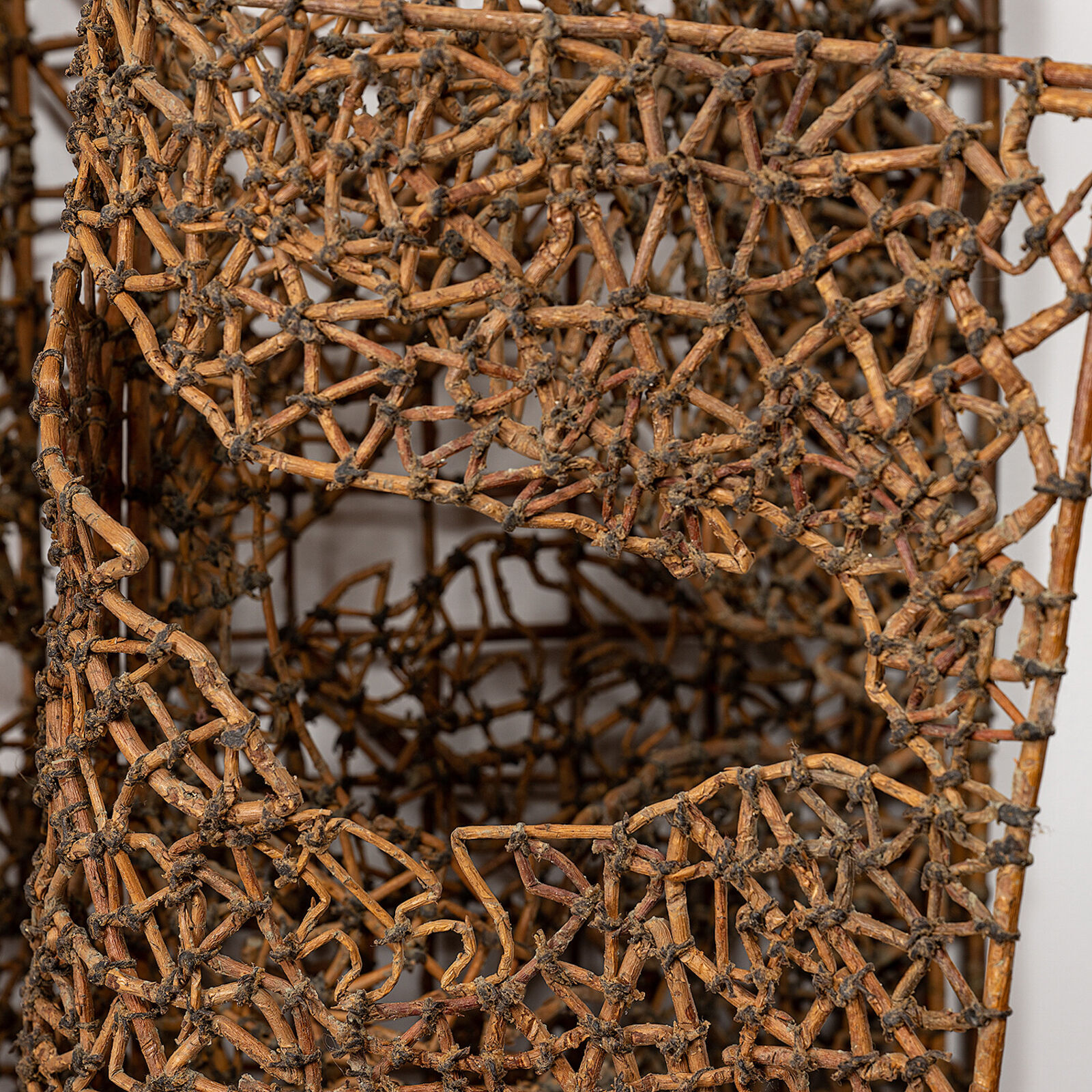 A sculptural book made of woven twigs sits on a white surface beneath a window.