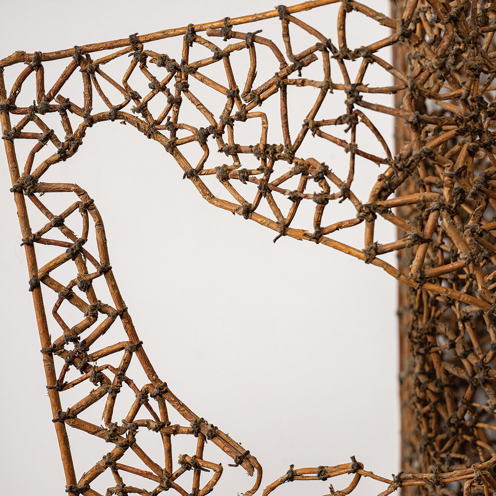 A sculptural book made of woven twigs sits on a white surface beneath a window.