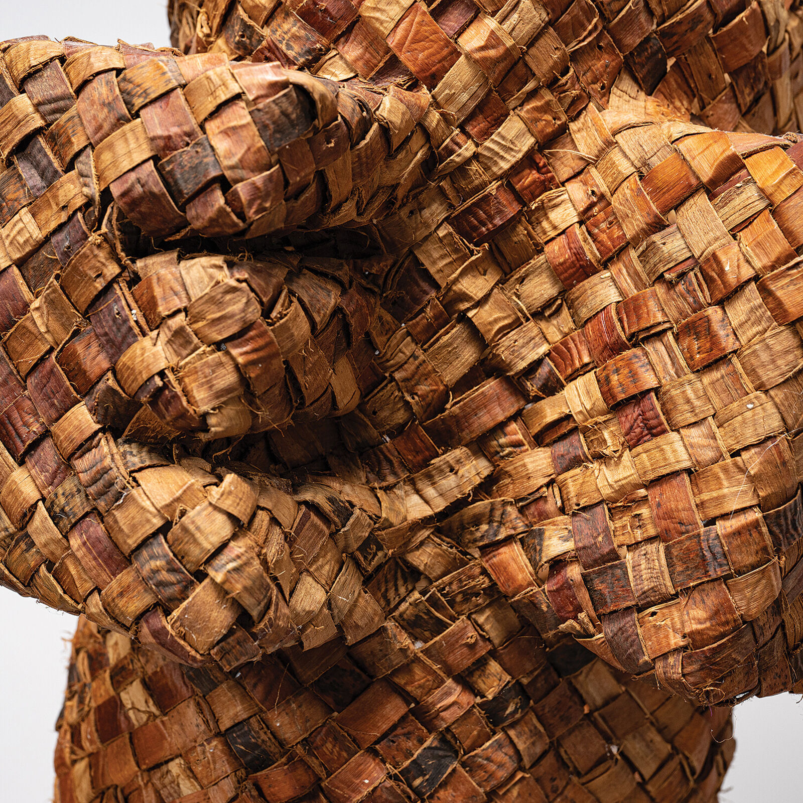A pair of woven basket sculptures shaped like stylized figures with raised arms, displayed on a white pedestal.