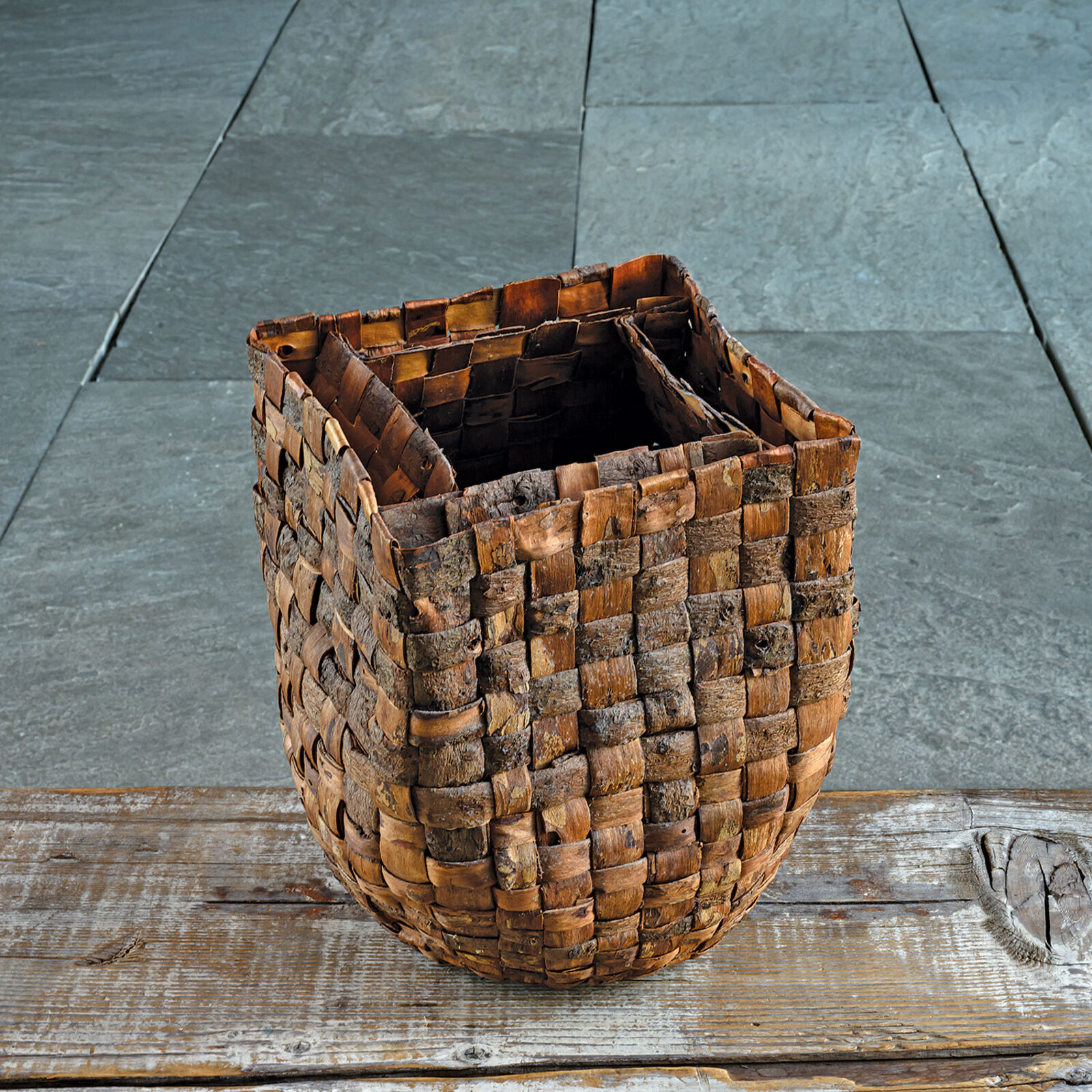 A woven basket sits on a weathered wooden plank against a slate background.