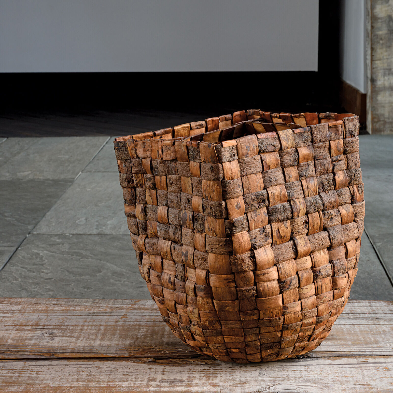 A woven basket sits on a weathered wooden plank against a slate background.