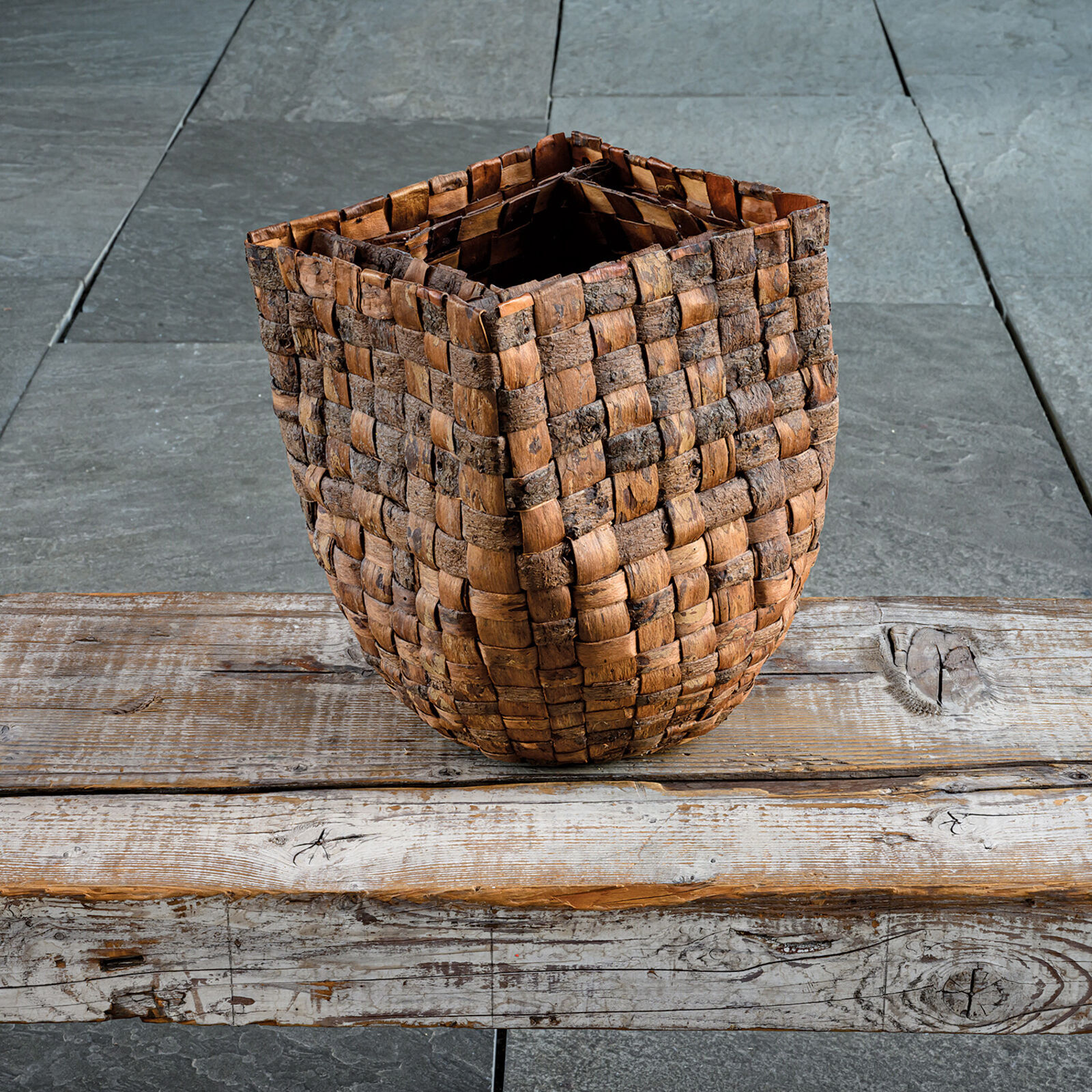 A woven basket sits on a weathered wooden plank against a slate background.