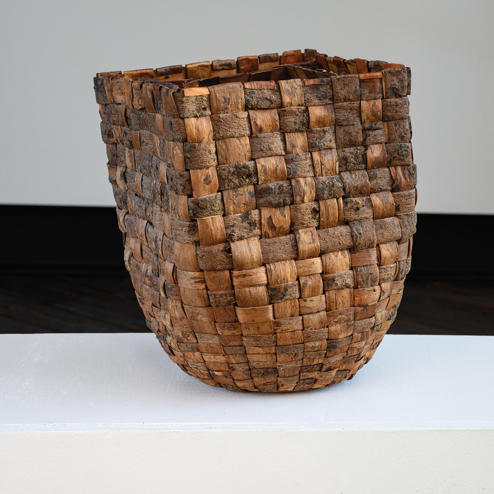 A woven basket sits on a weathered wooden plank against a slate background.