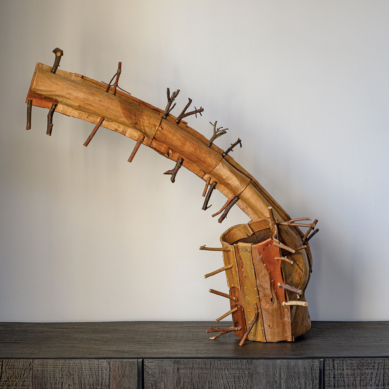 A rustic wooden sculpture resembling a stylized horn or branch, adorned with numerous small twigs.