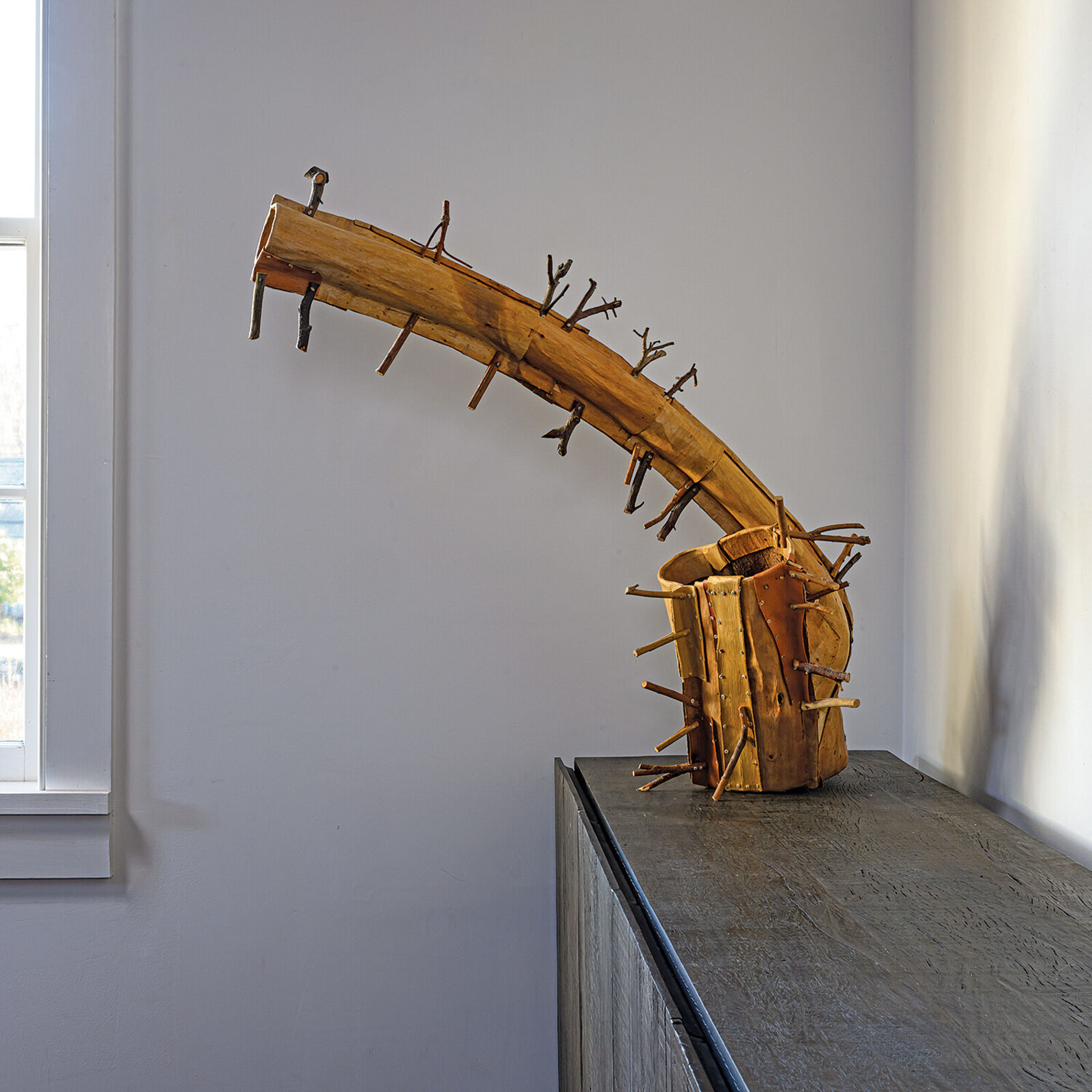 A rustic wooden sculpture resembling a stylized horn or branch, adorned with numerous small twigs.