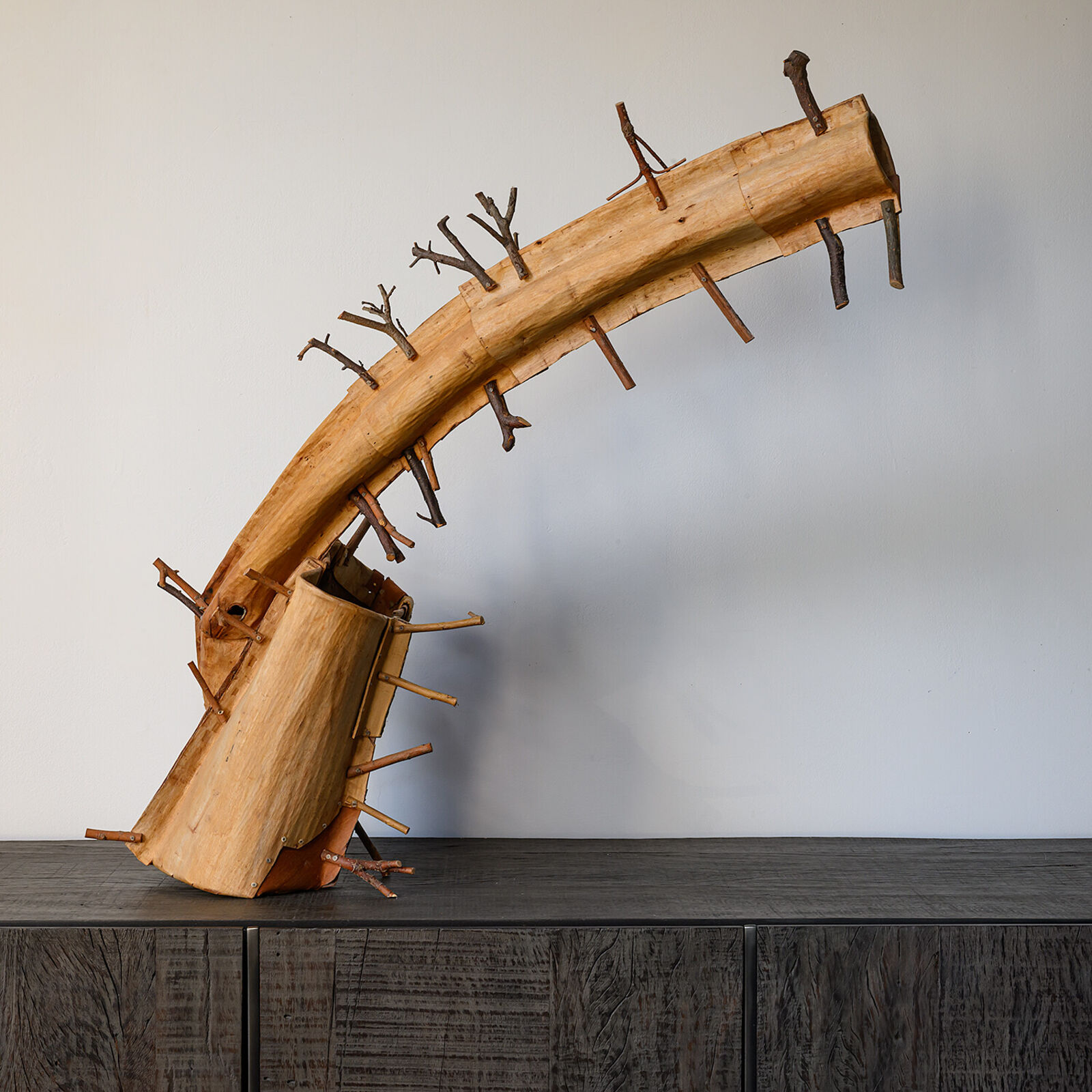 A rustic wooden sculpture resembling a stylized horn or branch, adorned with numerous small twigs.