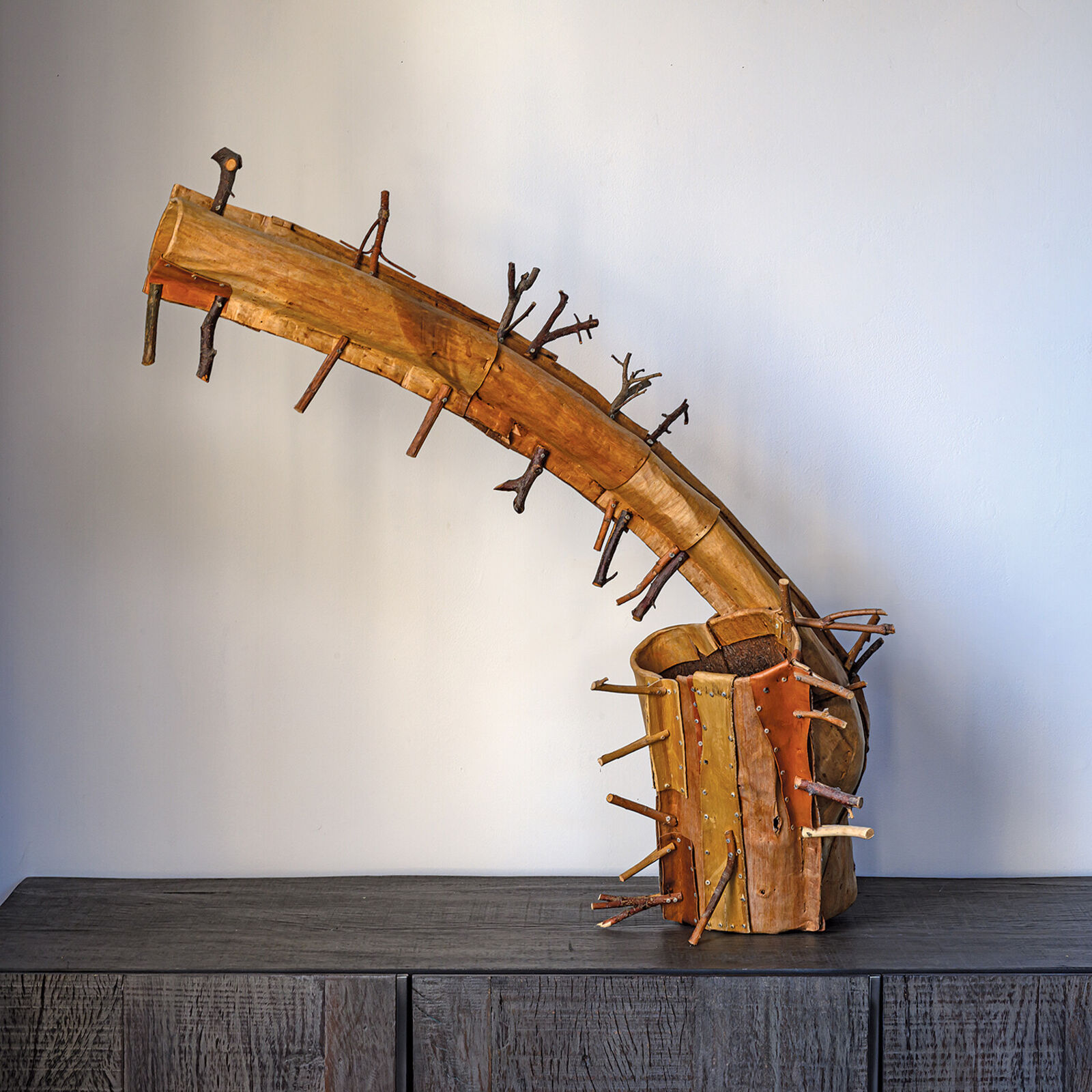 A rustic wooden sculpture resembling a stylized horn or branch, adorned with numerous small twigs.