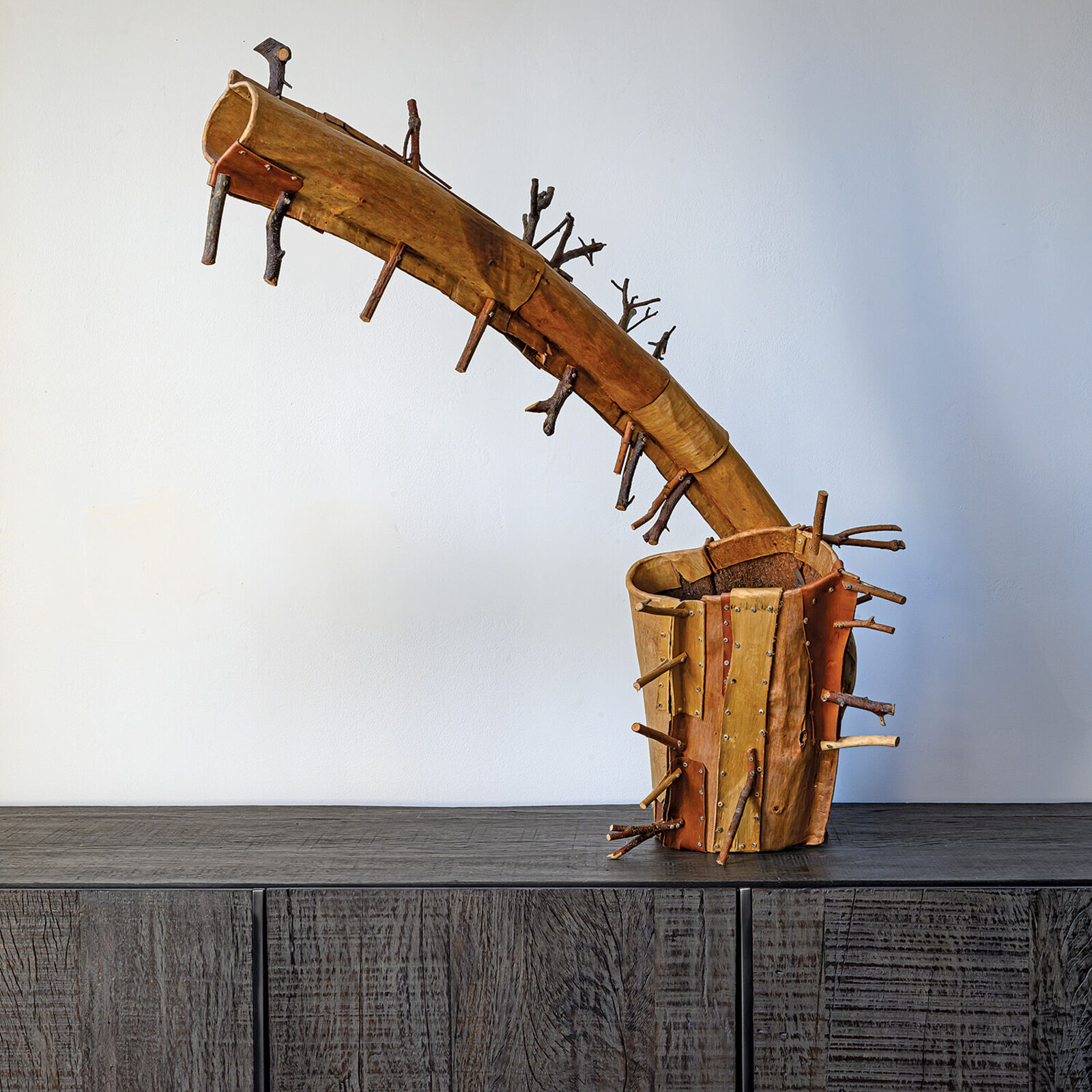 A rustic wooden sculpture resembling a stylized horn or branch, adorned with numerous small twigs.