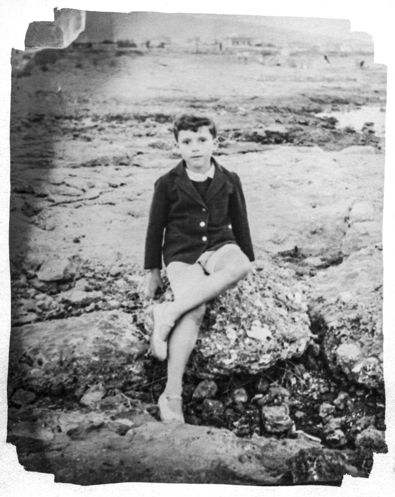 A young boy sitting on a rock on the beach.