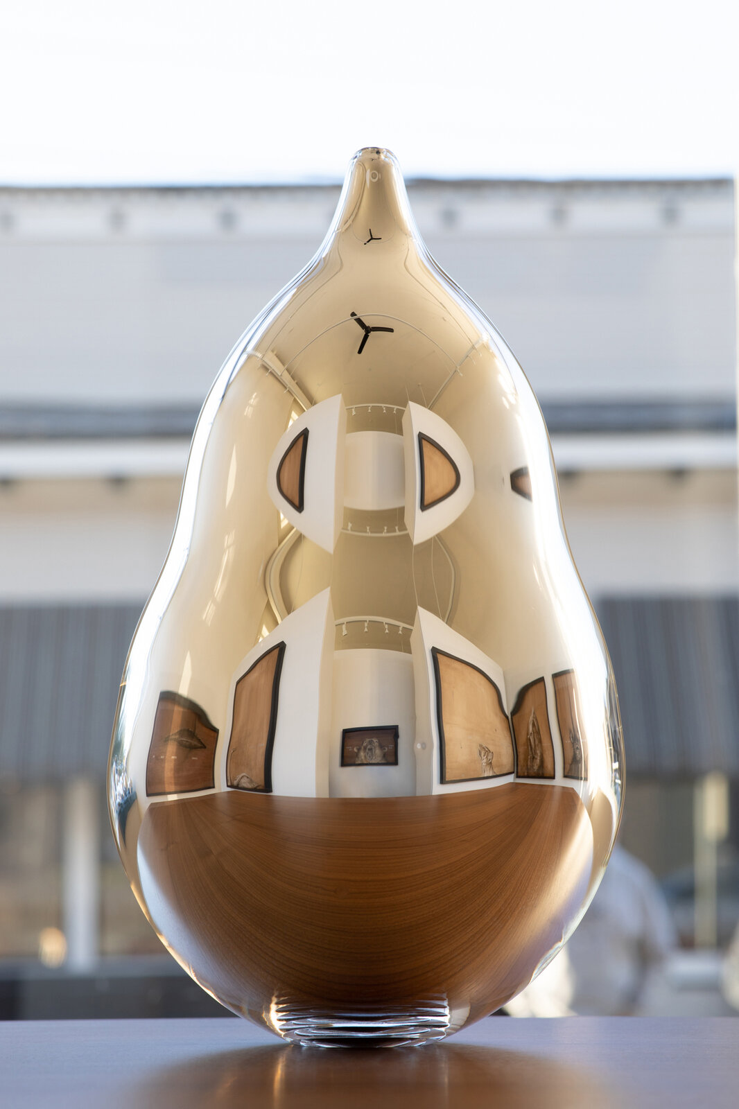 A golden, teardrop-shaped sculpture with a reflective surface and internal wooden inlays.