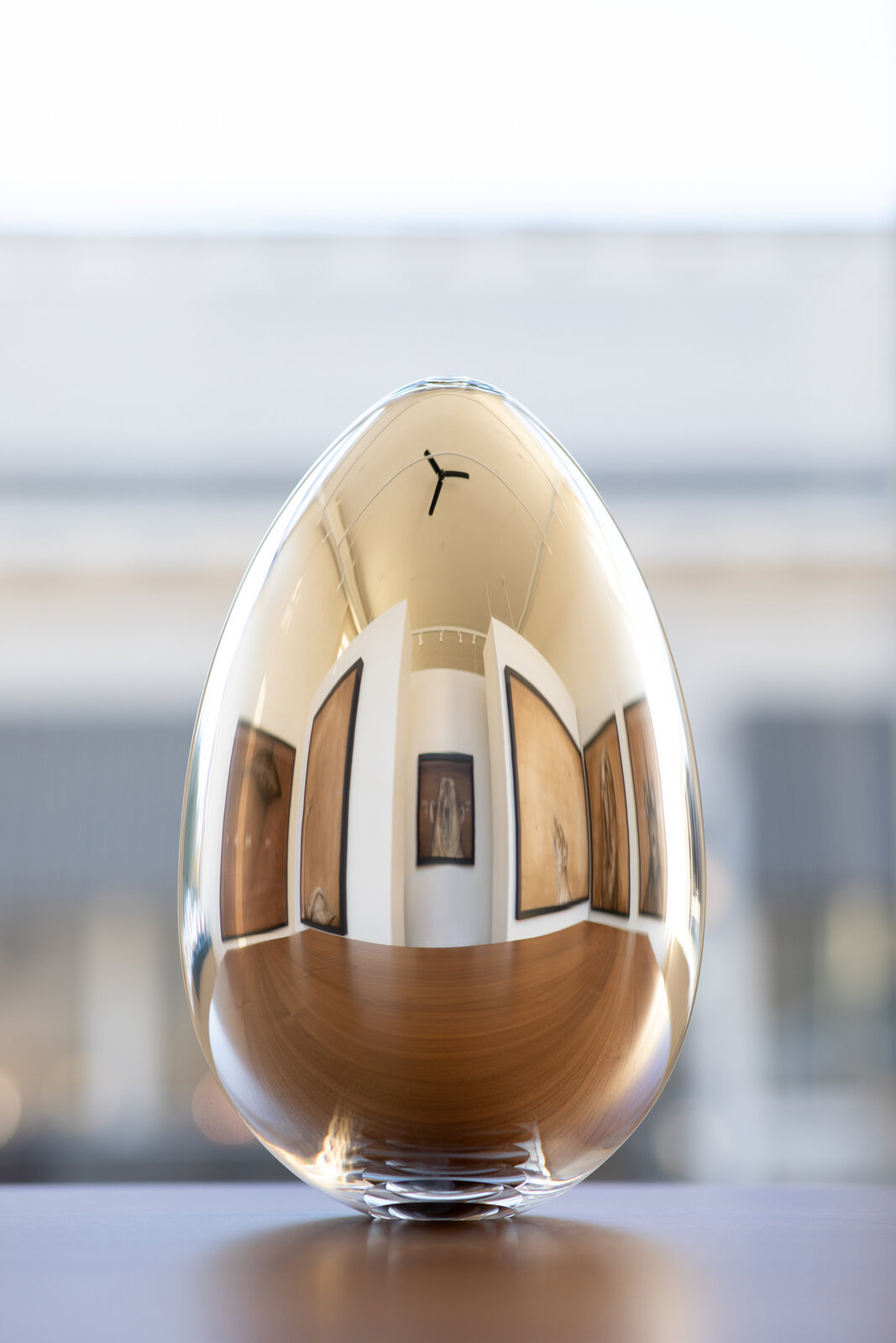 A reflective glass egg-shaped object captures a gallery interior in its curved surface.