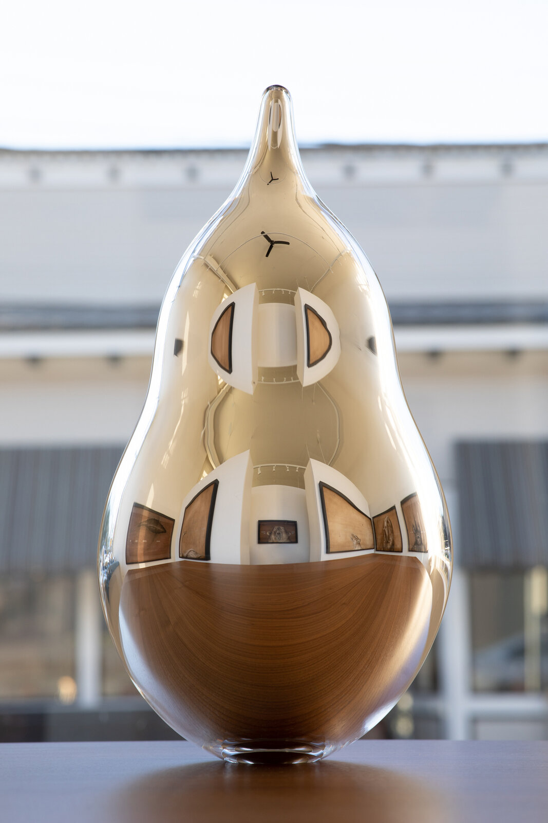 A golden, pear-shaped sculpture with a wooden base and geometric inlays.