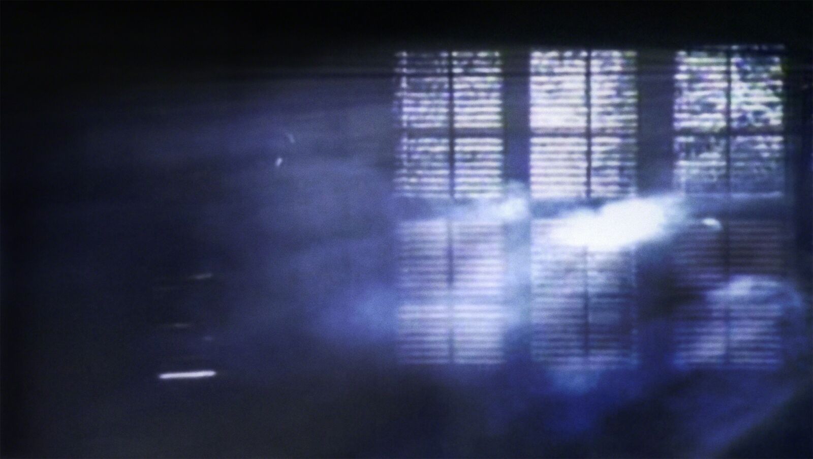 A grainy, atmospheric shot of a grid-like structure illuminated by cool blue light.