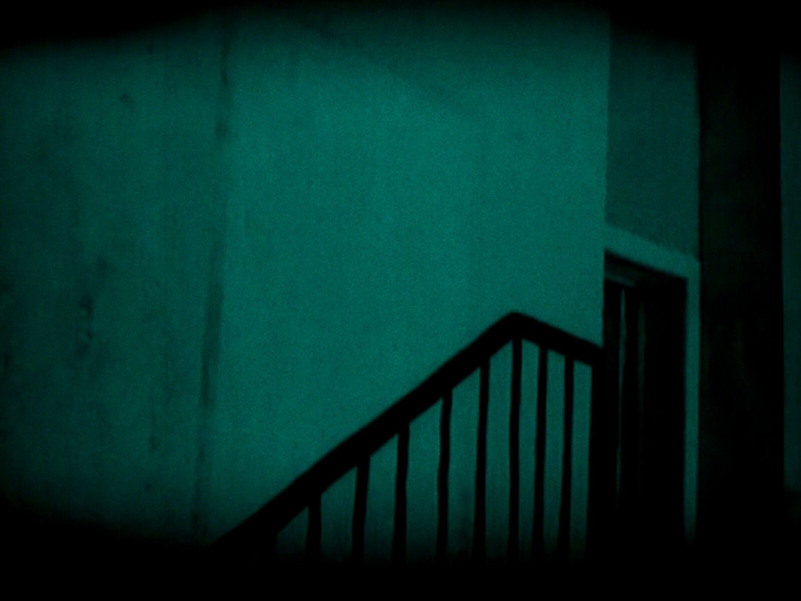A moody, teal-tinted interior shot of a staircase railing against a textured wall.