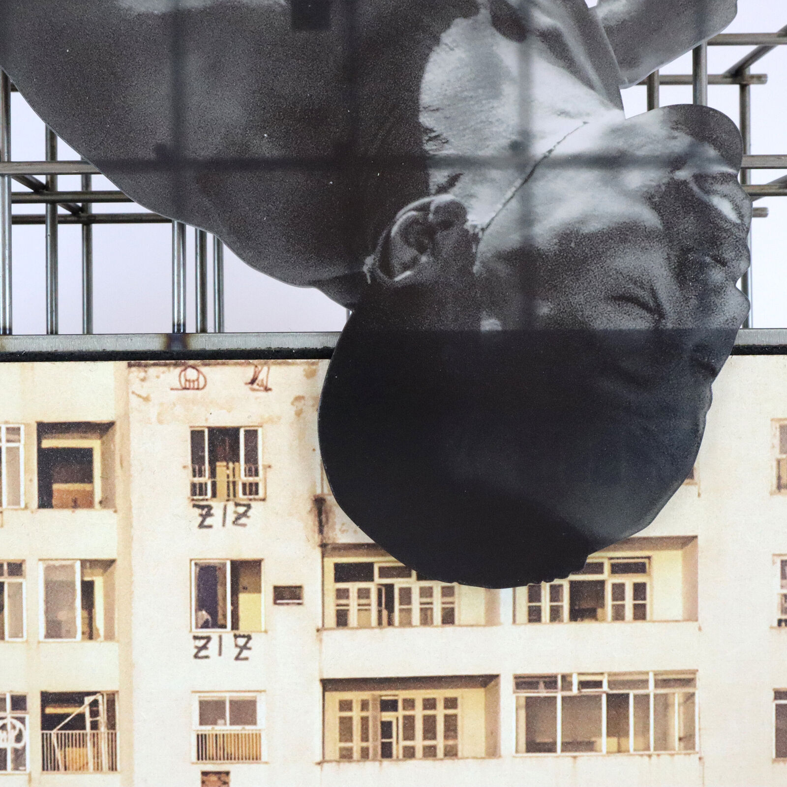 A miniature architectural model of a high-rise building topped by a suspended, contorted human figure.