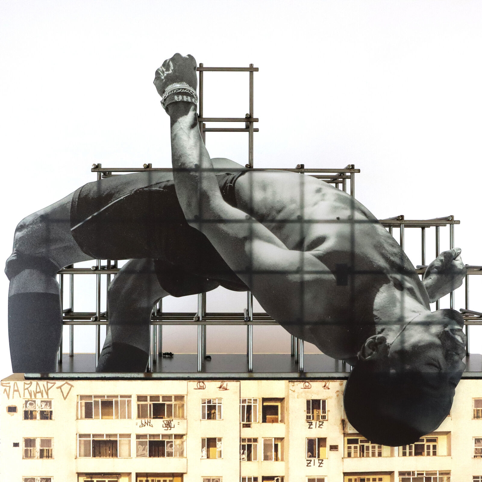 A miniature architectural model of a high-rise building topped by a suspended, contorted human figure.