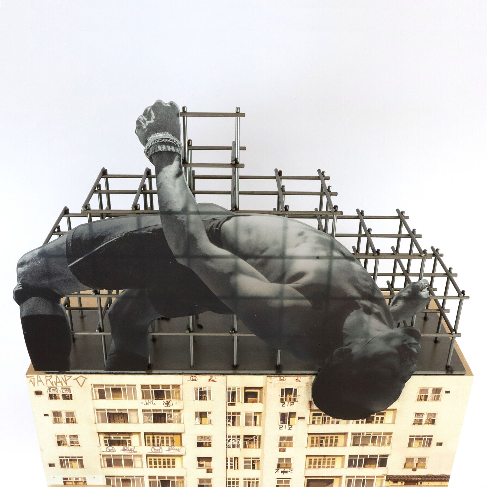 A miniature architectural model of a high-rise building topped by a suspended, contorted human figure.