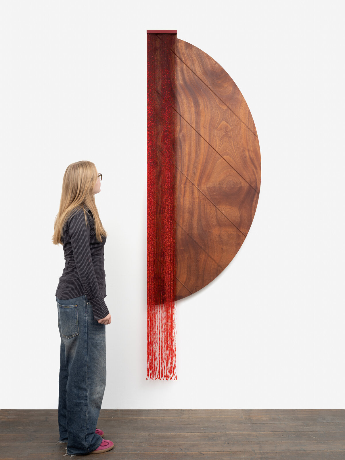 A minimalist wall piece featuring a wooden semi-circle and a red woven element.