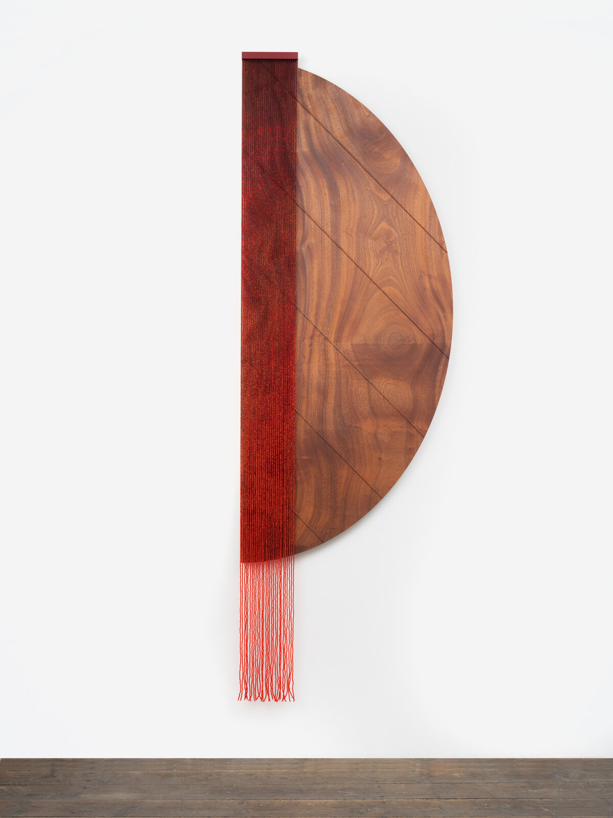 A minimalist wall piece featuring a wooden semi-circle and a red woven element.