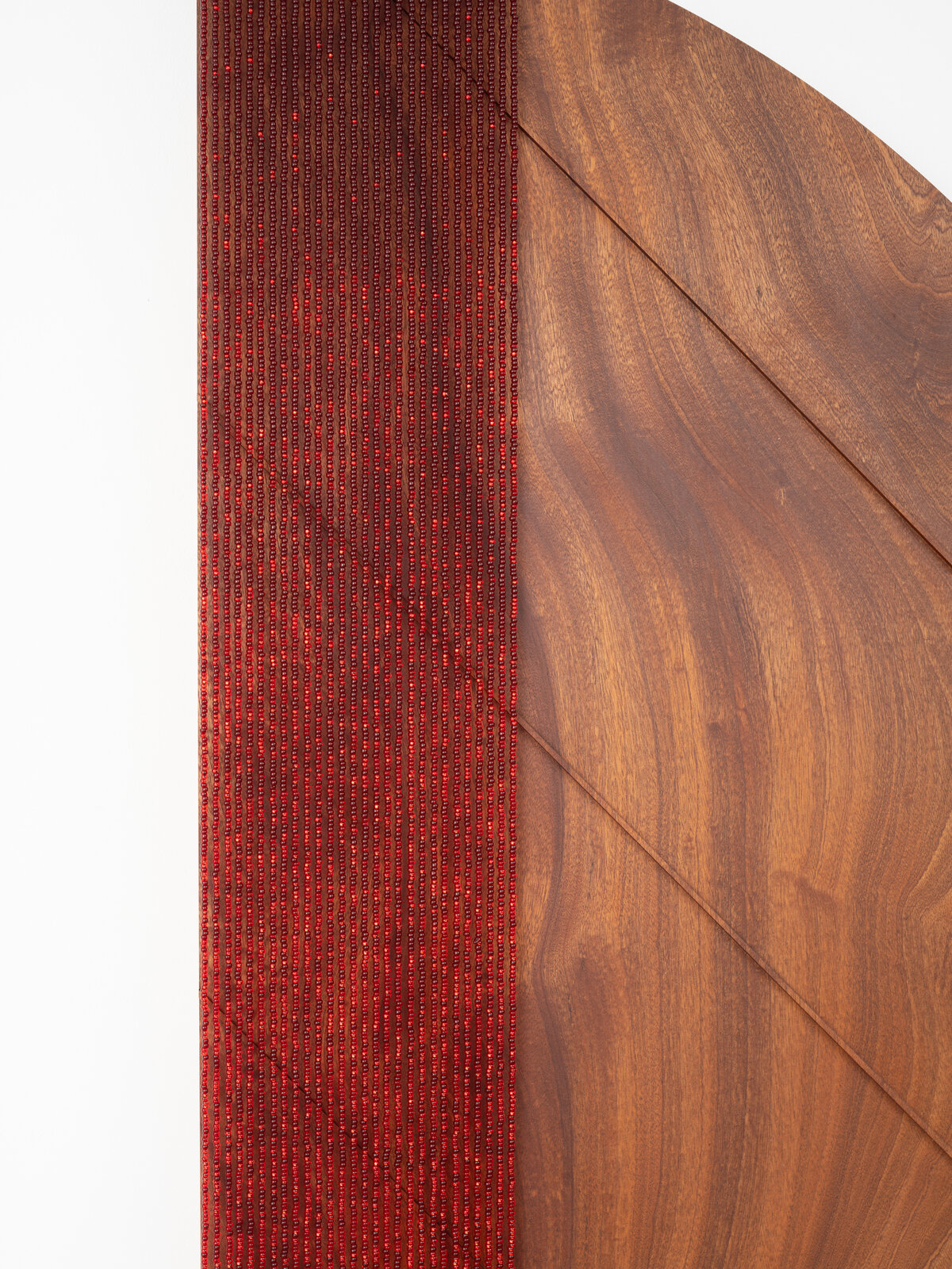 A minimalist wall piece featuring a wooden semi-circle and a red woven element.