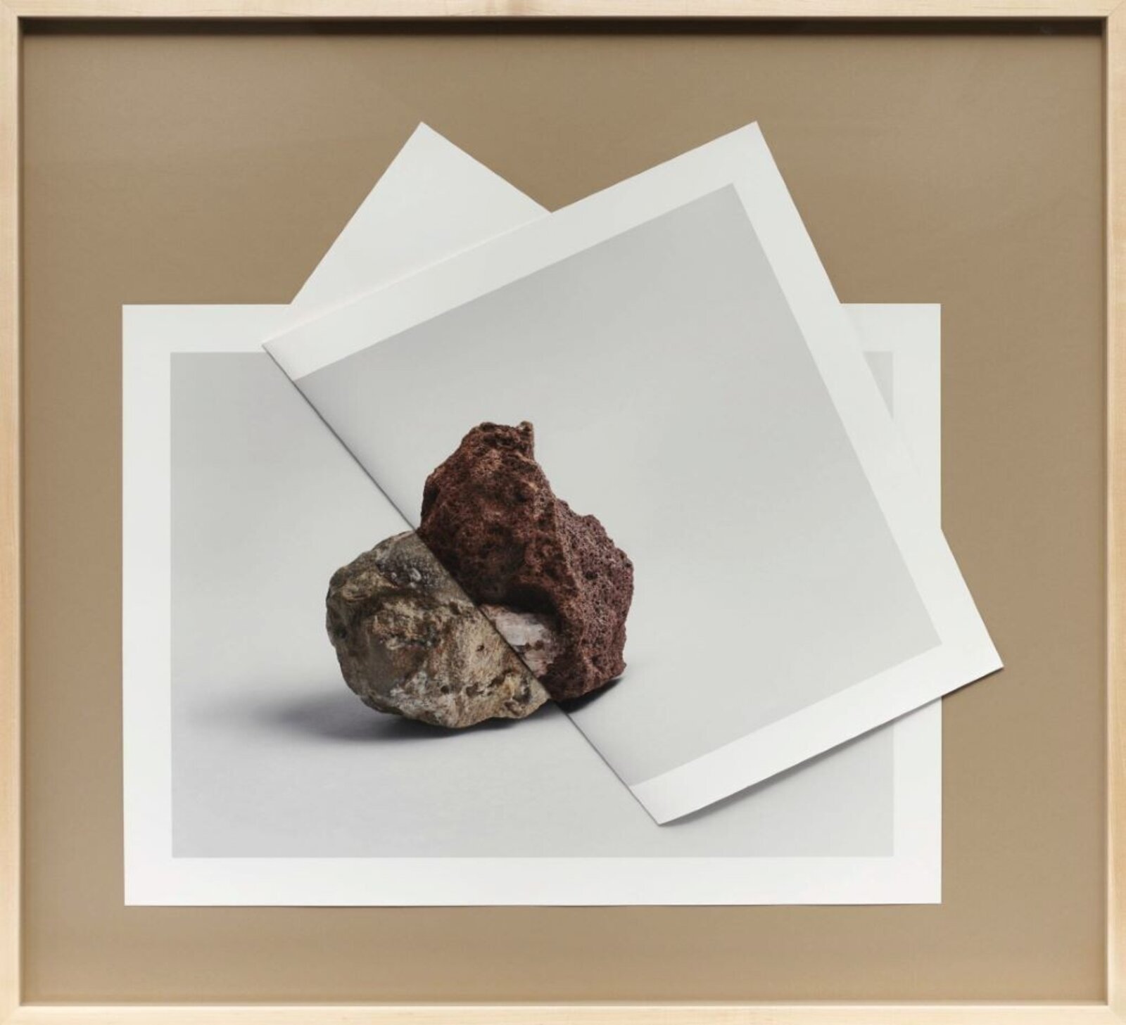 A framed photograph of two rocks resting on a white surface, layered over printed paper.